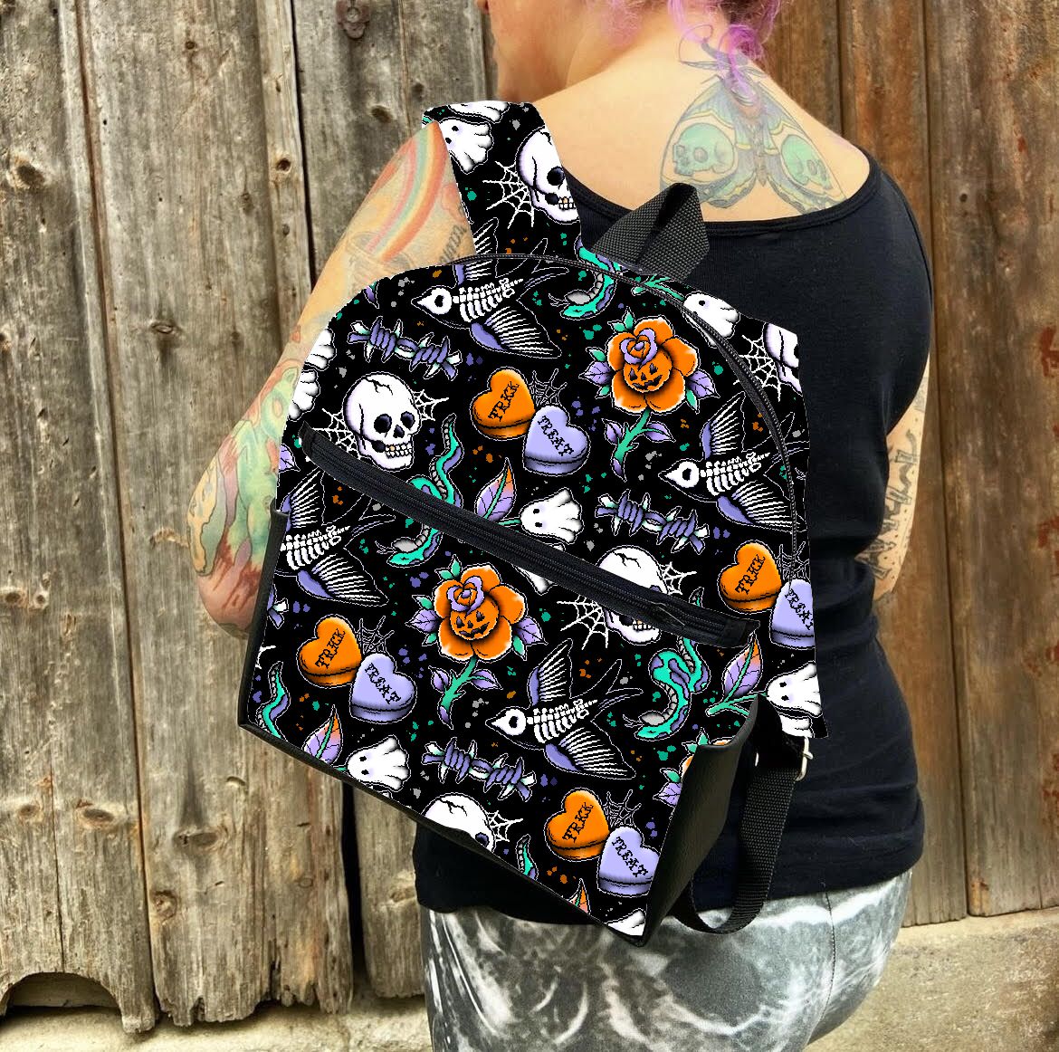 Mochila preta com padrão colorido de caveiras, corações e flores usada por pessoa com tatuagens