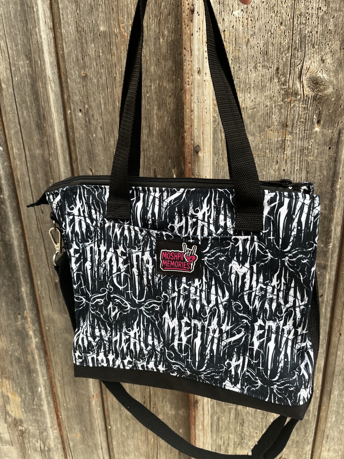 Mala preta e branca com padrão e etiqueta MOSHPIT MEMORIES pendurada em fundo de madeira
