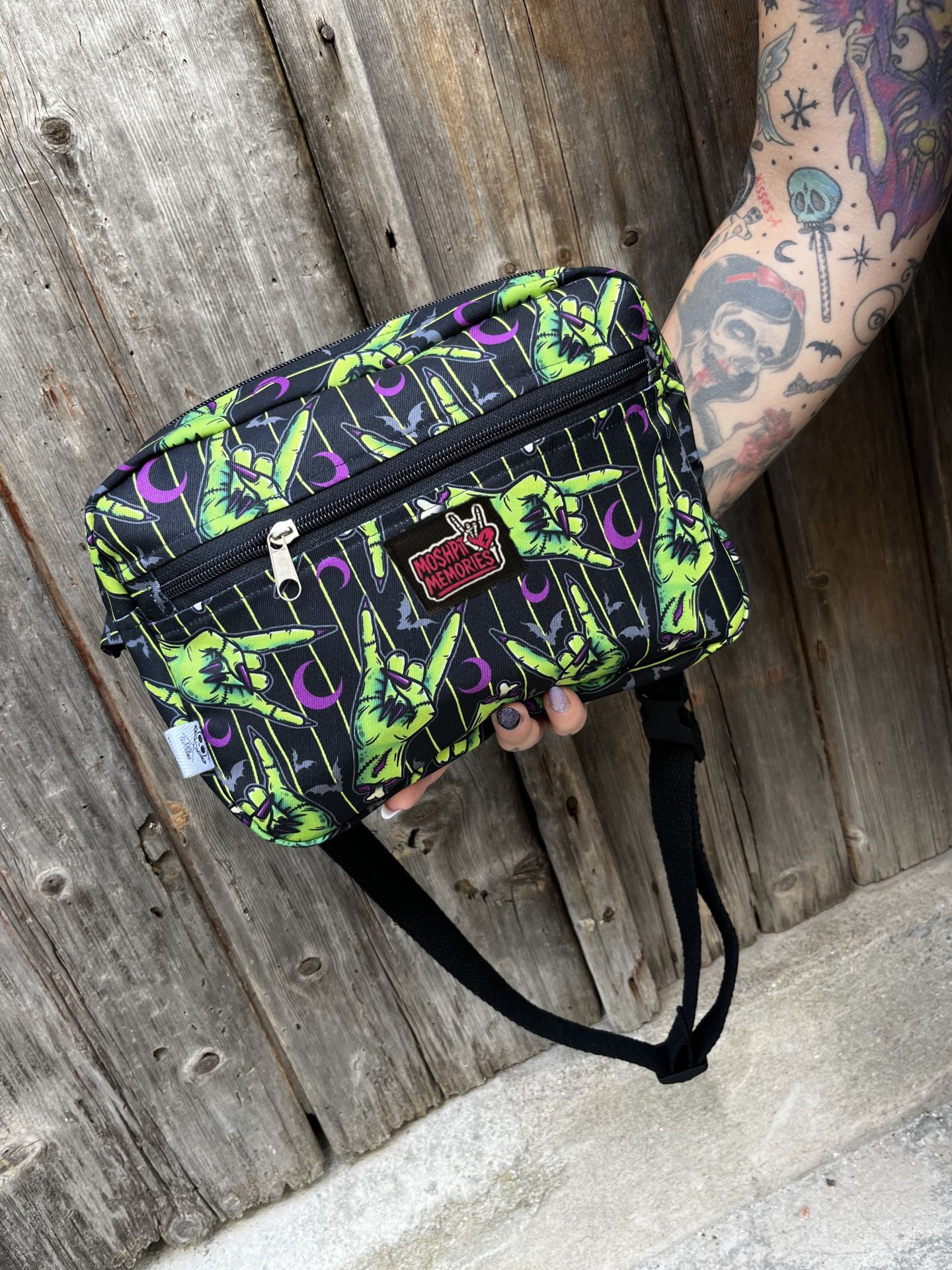 Bolsa tiracolo preta com padrão de mãos verdes em gesto rock e etiqueta MOSHPIT MEMORIES