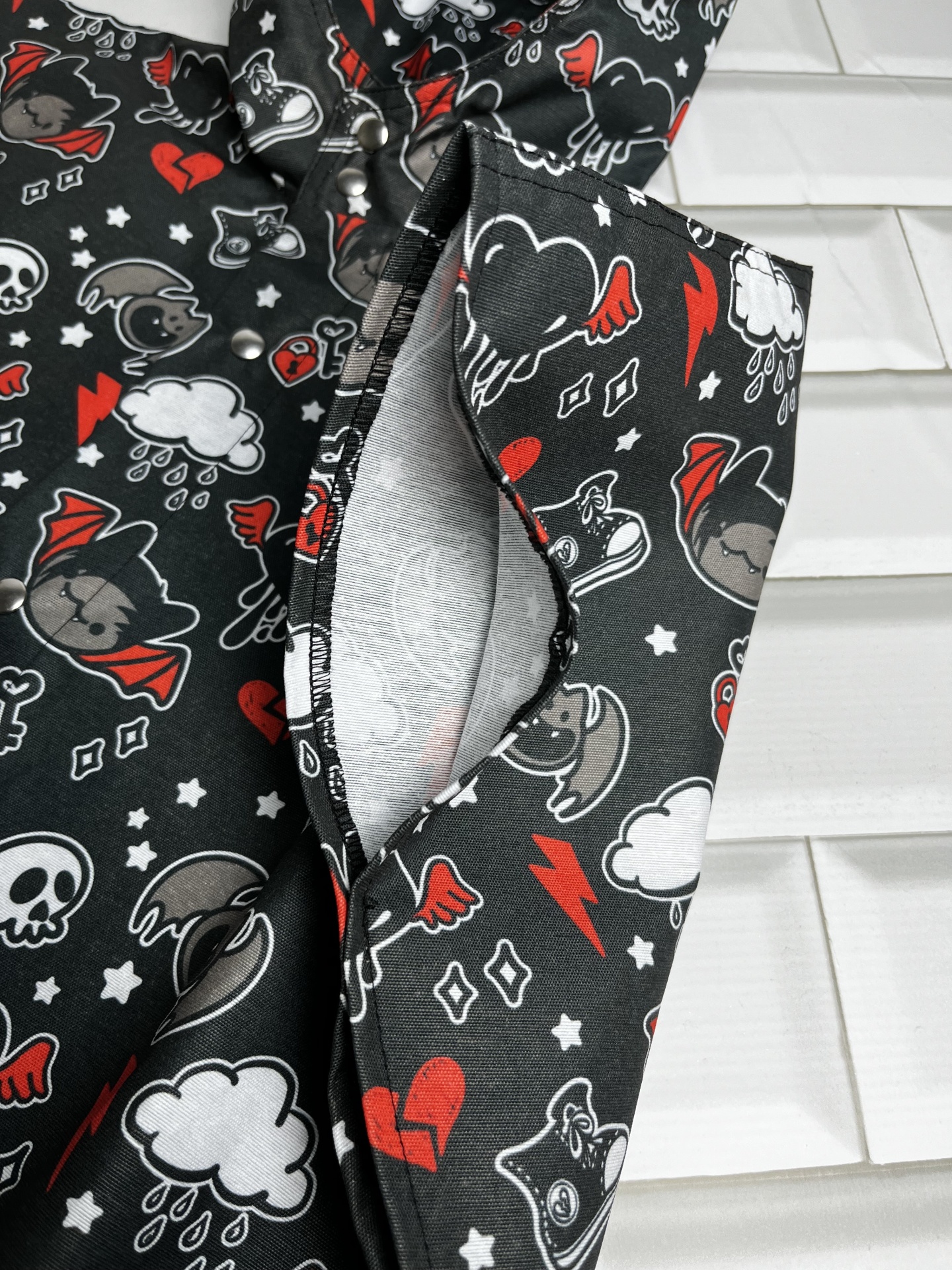 Tecido preto com padrão colorido de caveiras e morcegos, roupa com interior cinzento