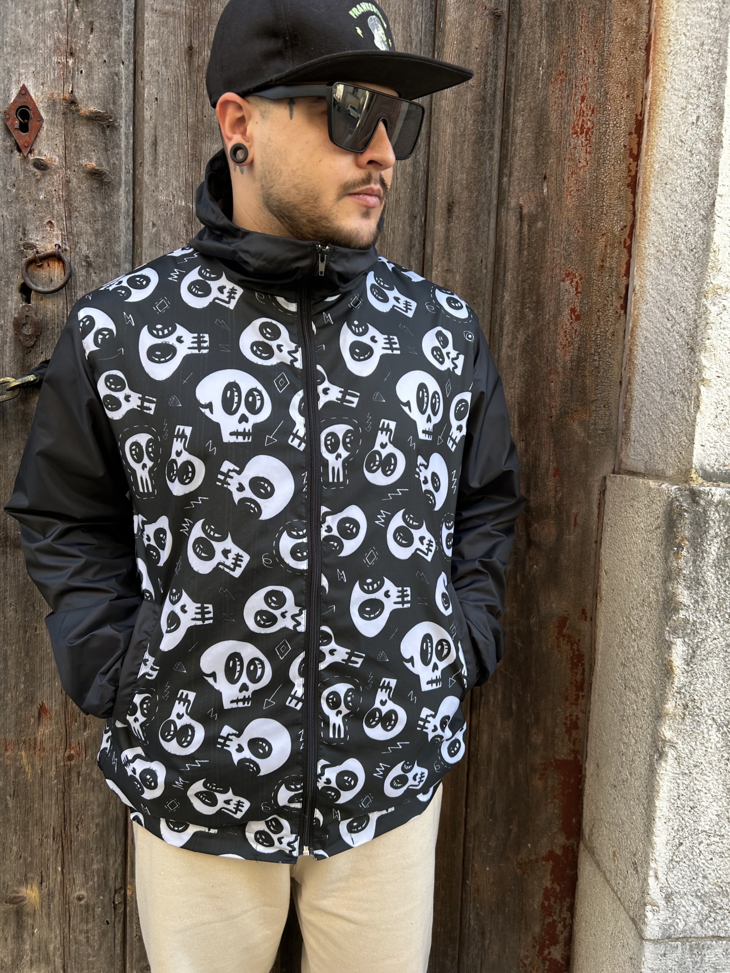 Casaco preto e branco com padrão de caveiras usado por homem junto a porta de madeira
