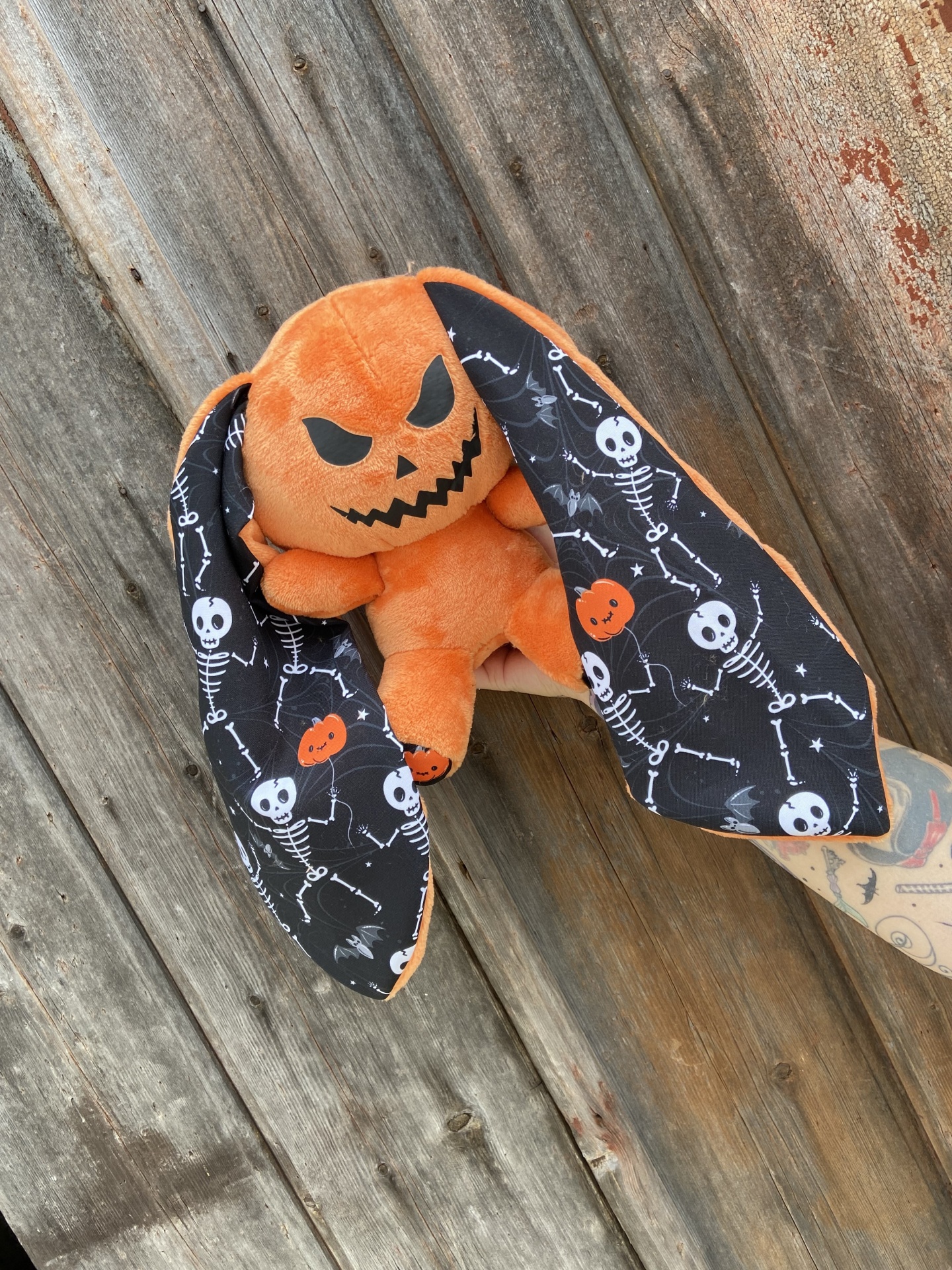 Boneco de peluche laranja com cabeça em forma de abóbora e orelhas longas com padrões de esqueletos