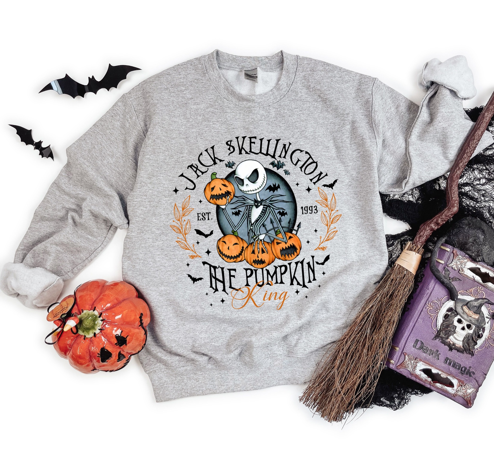 Sweatshirt cinzenta com estampado de personagem e texto Halloween, rodeada de adereços festivos