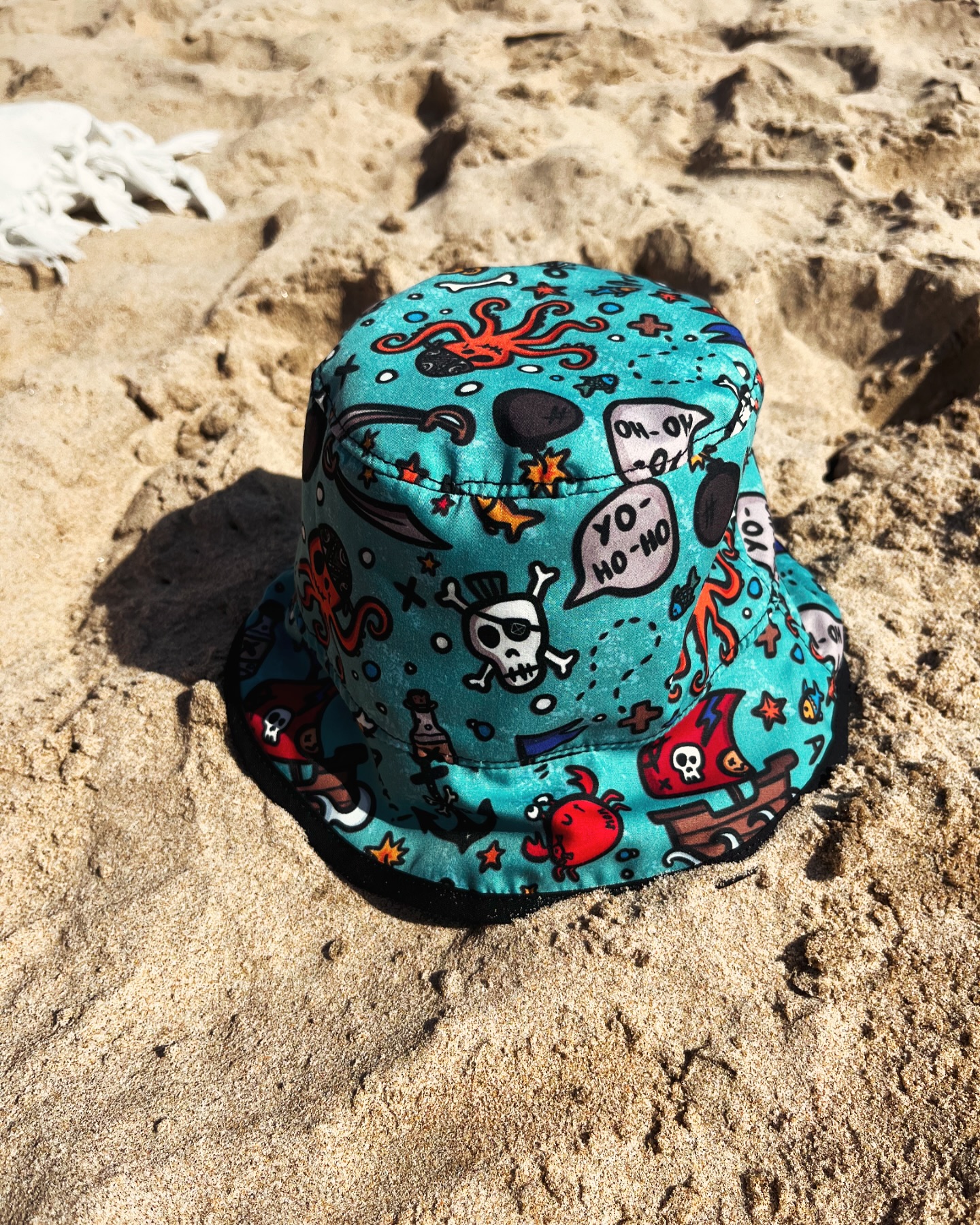 Chapéu tipo pescador colorido com desenhos de pirata na areia da praia