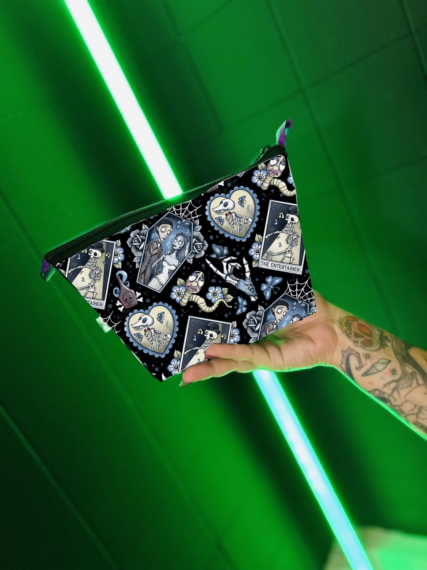 Bolsa pequena com padrão de tarô em fundo preto segurada por mão tatuada em ambiente iluminado por luz verde