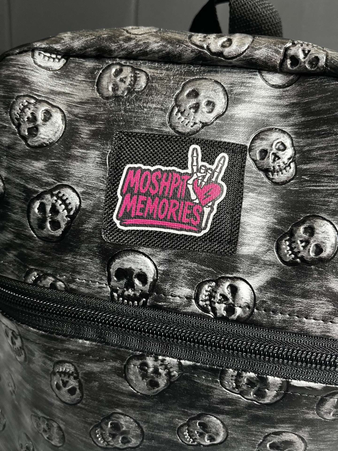 Mochila preta com caveiras e etiqueta MOSH PIT MEMORIES