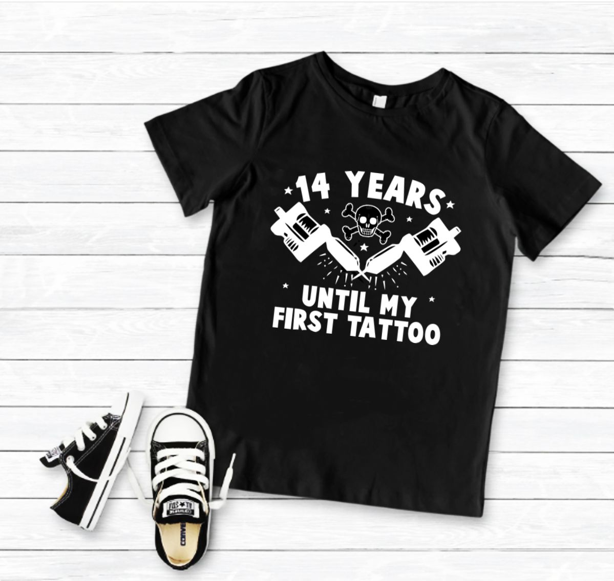T-shirt preta com estampa branca de tatuagens e texto, com sapatilhas pretas e brancas ao lado