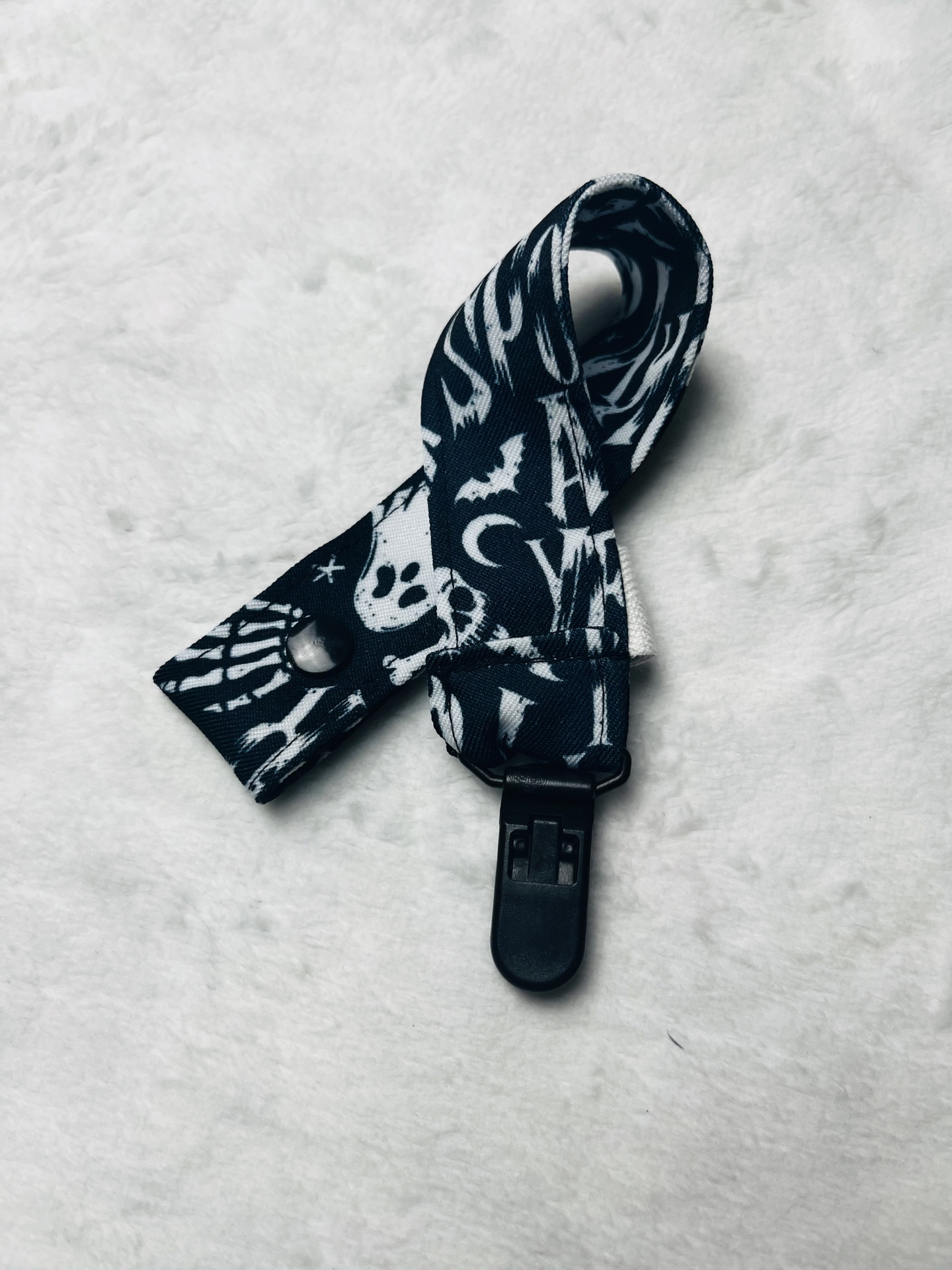 Tira preta com estampas brancas e fivela preta sobre superfície branca peluda