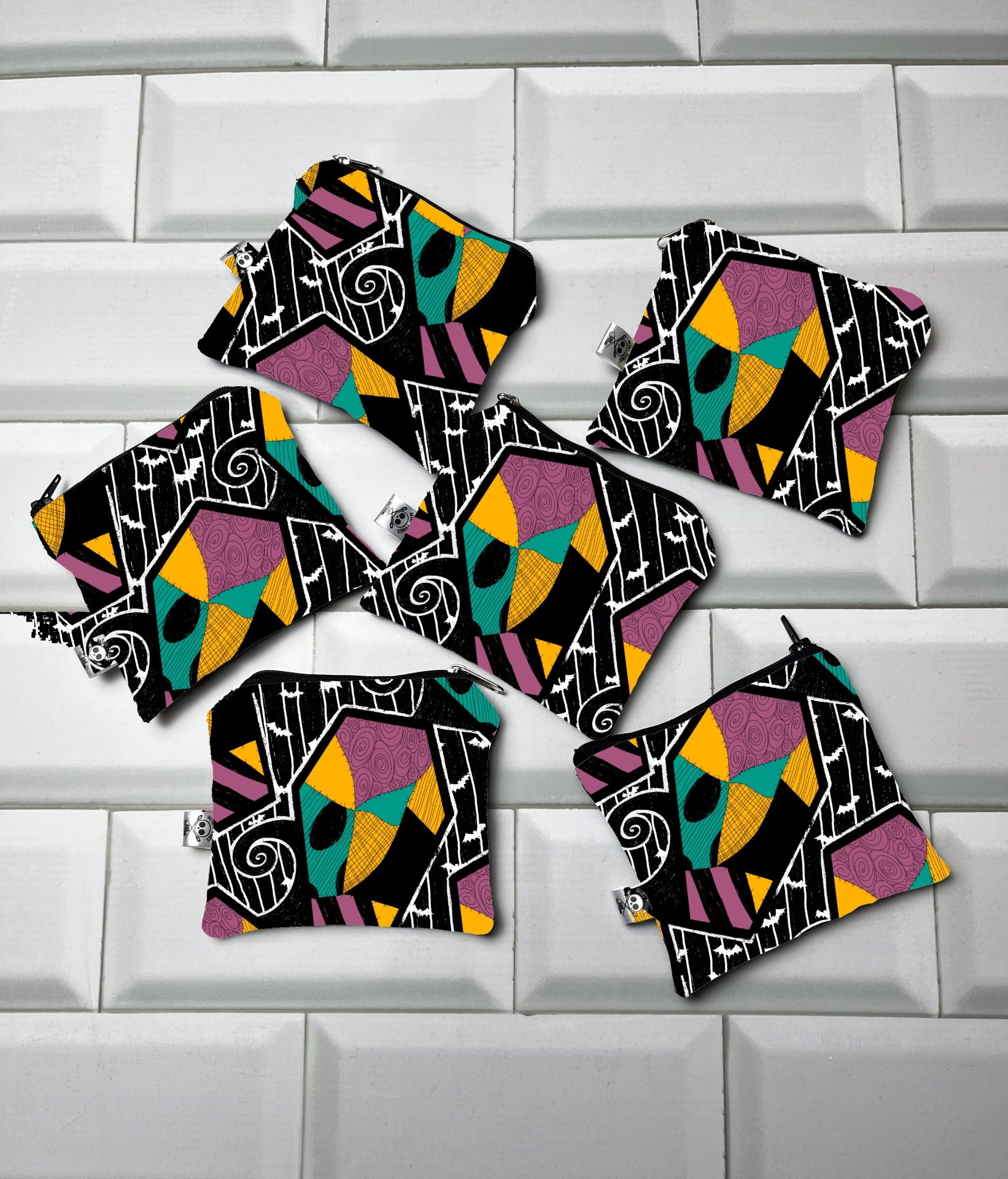 Seis pequenas bolsas de tecido coloridas com padrão geométrico sobre fundo de azulejos brancos