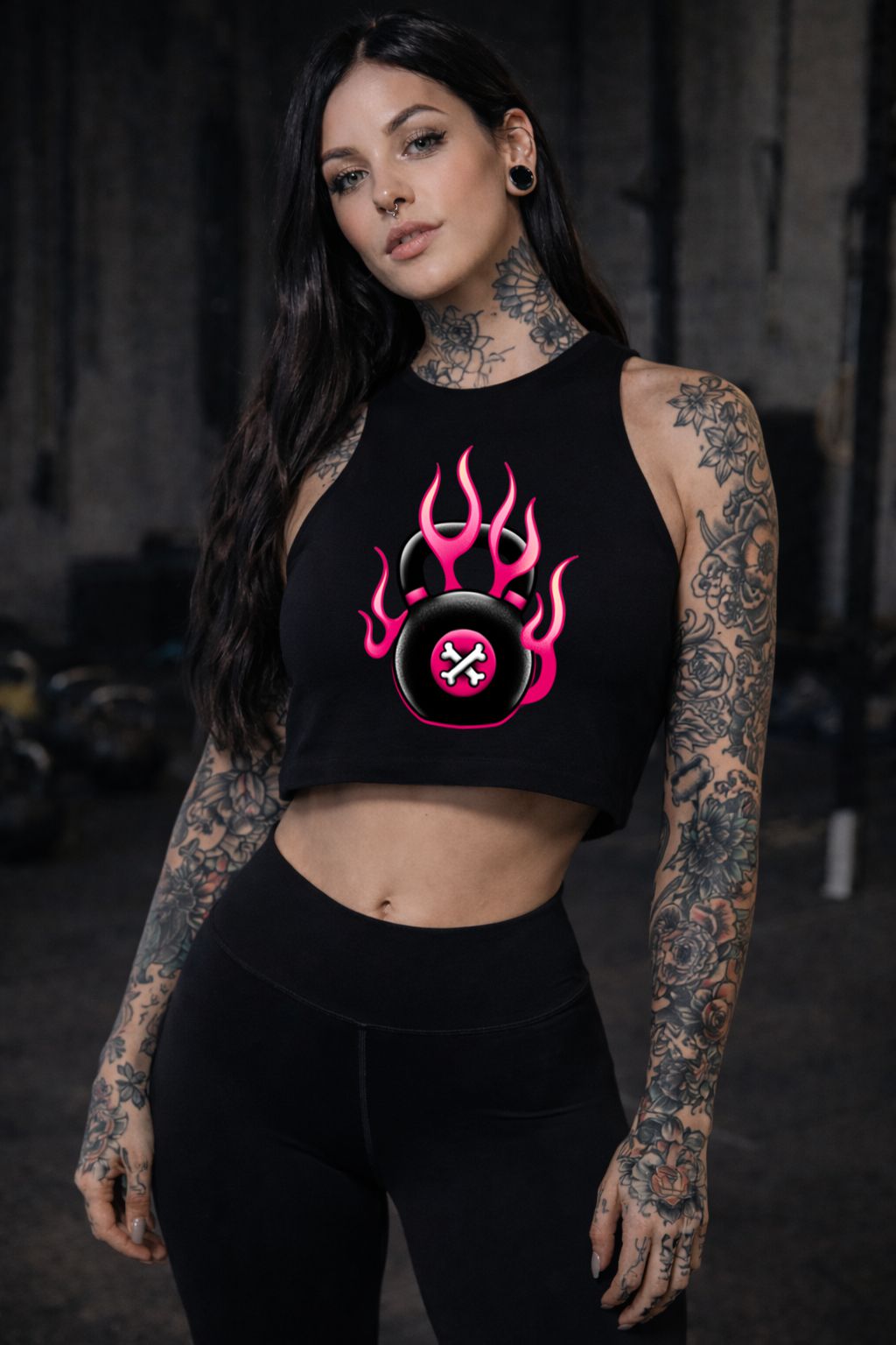 Mulher com top cropped preto estampado e leggings pretas num ginásio escuro.