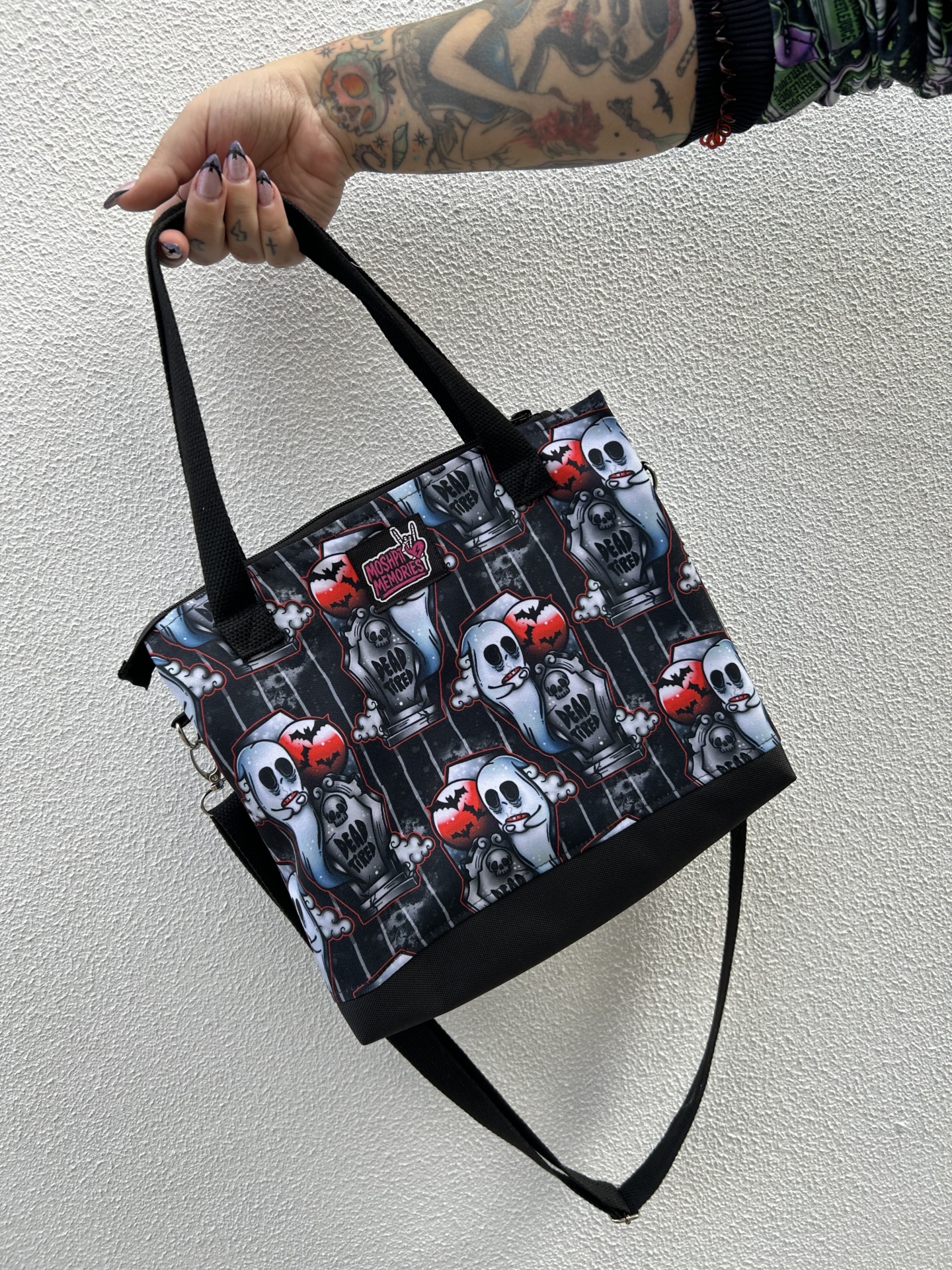 Bolsa estampada com fantasmas, lápides e morcegos, com alças pretas e etiqueta MOSHPIT MEMORIES