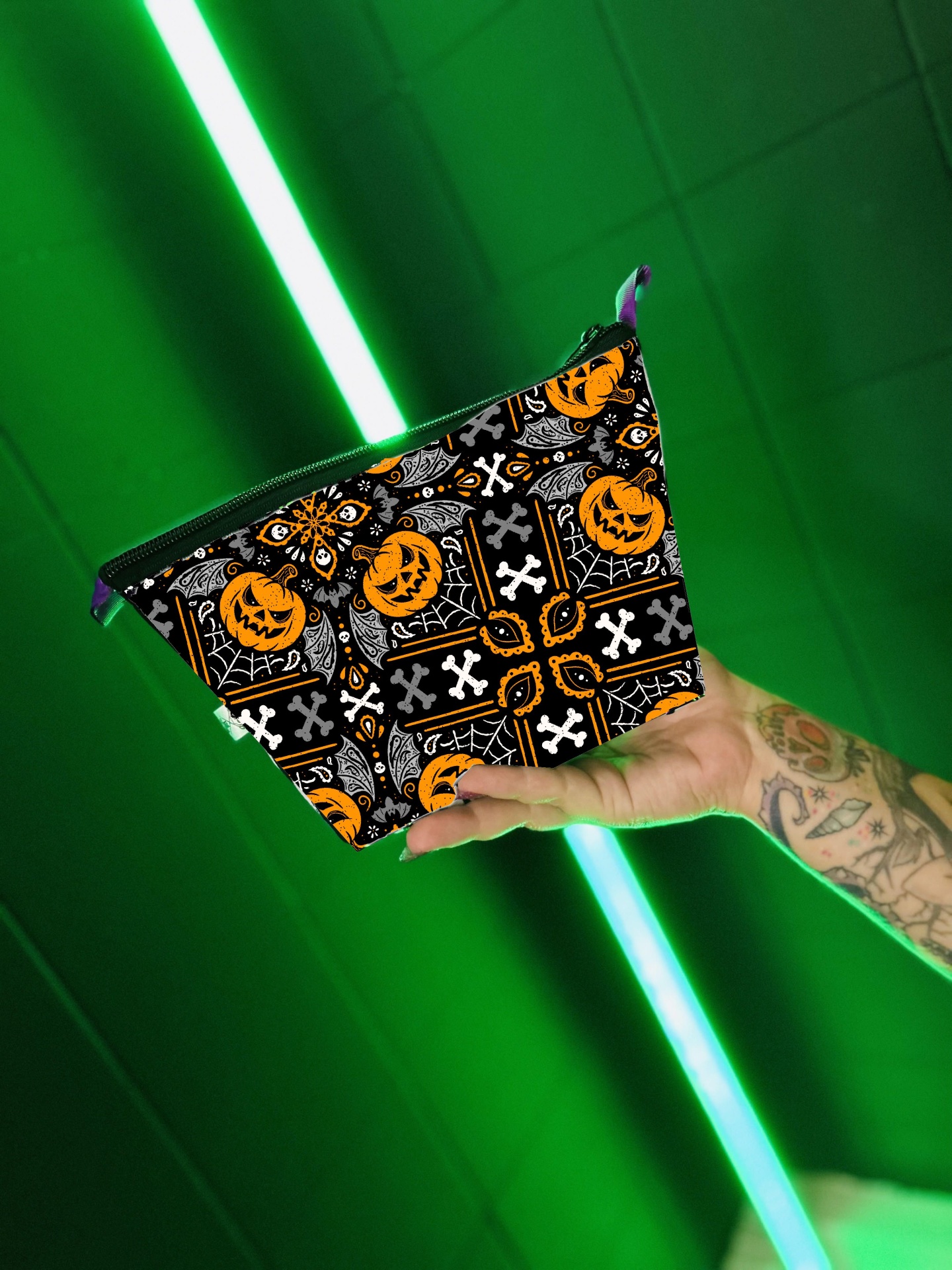 Necessaire triangular com padrão Halloween preto, branco e laranja em mão tatuada com fundo verde