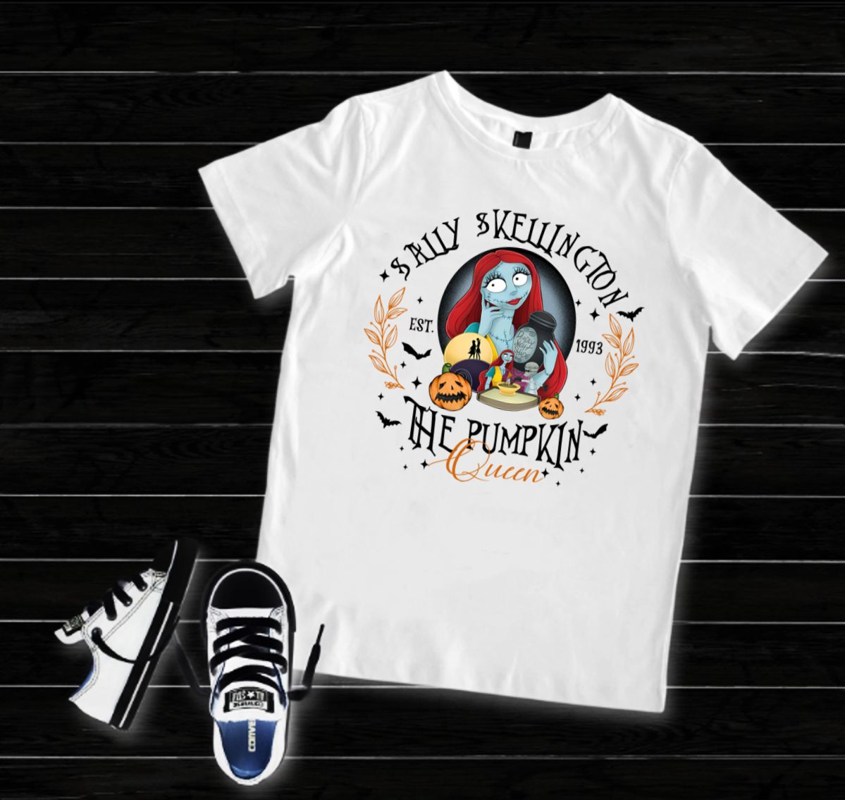 T-shirt branca com estampa da personagem Sally Skellington segurando abóboras e texto decorativo