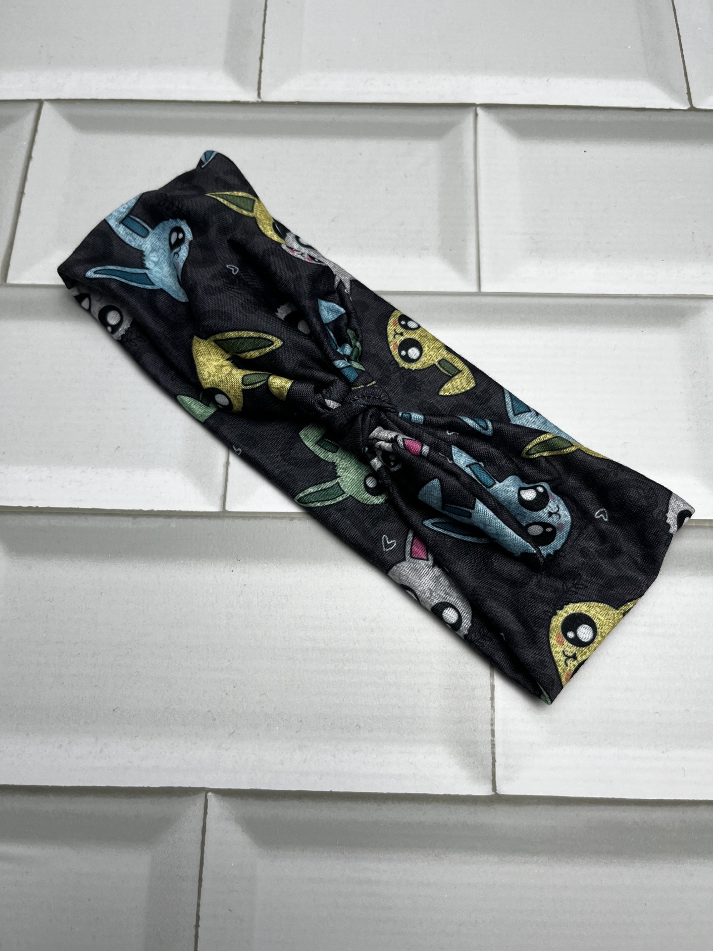 Faixa de cabelo preta com personagens cartoon coloridos sobre azulejos brancos