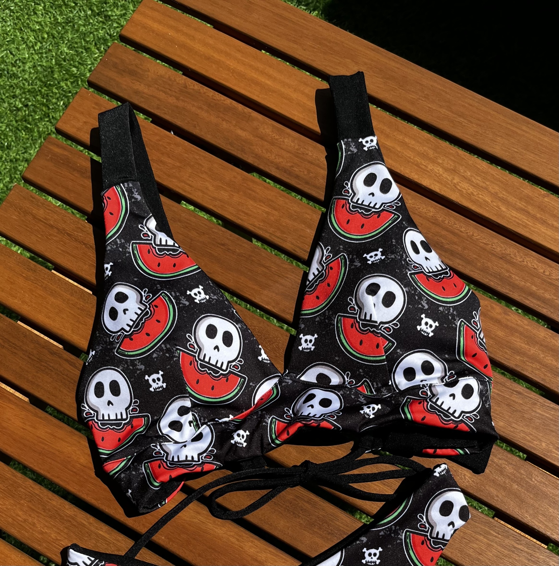 Top de biquíni preto com caveiras e melancias sobre madeira