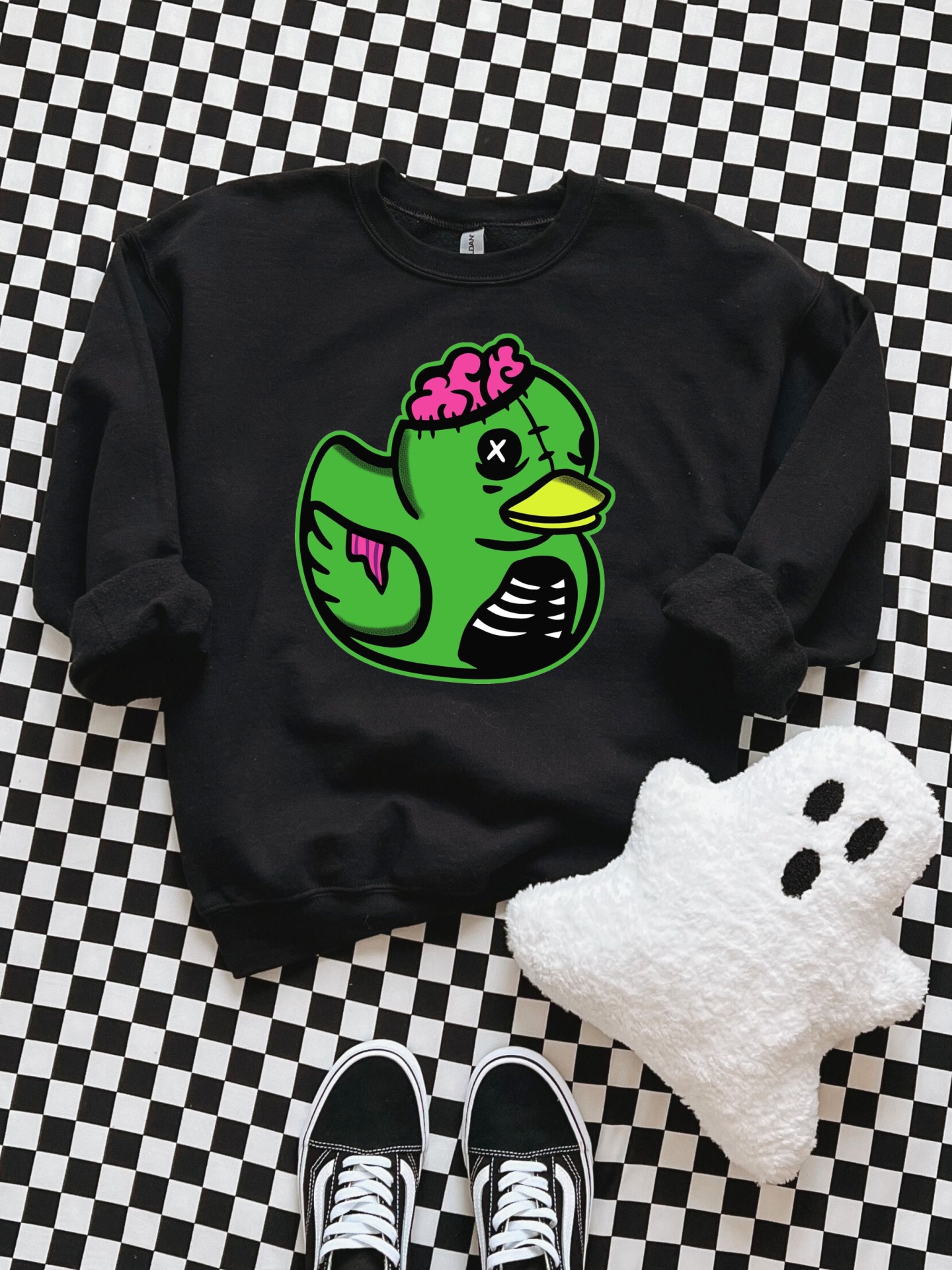 Sweatshirt preta com estampa de patinho zumbi verde e acessórios sobre fundo quadriculado