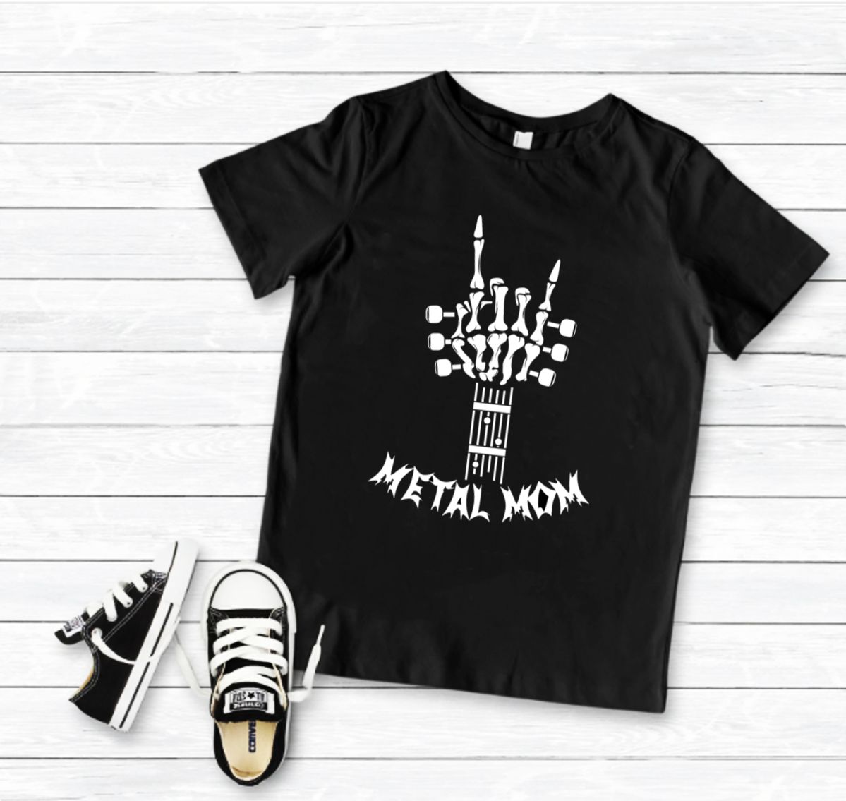 T-shirt preta com estampa de mão esqueleto e texto METAL MOM, com ténis pretos e brancos ao lado.