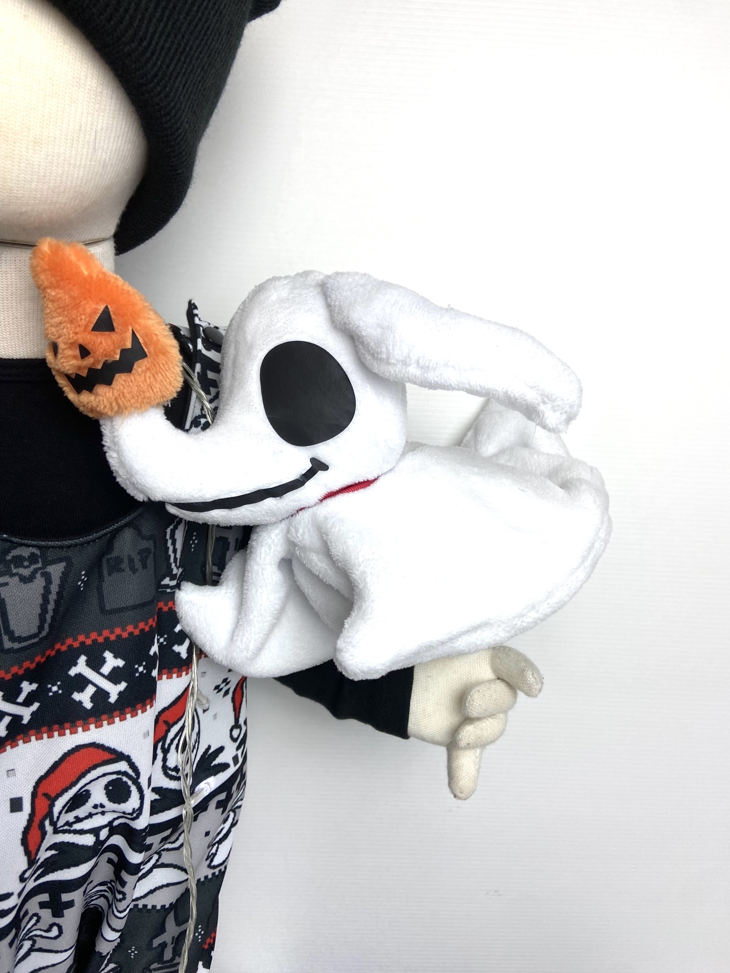 Boneco de pelúcia branco com nariz de abóbora laranja e roupas com padrão de Halloween