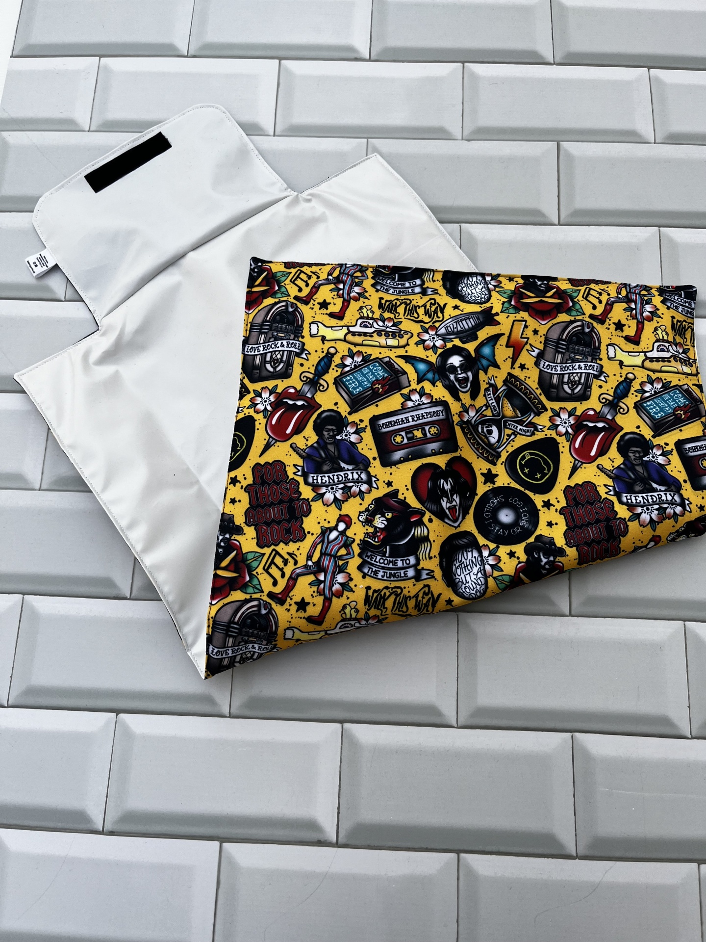 Almofada colorida com padrão de caveiras e fitas cassete sobre superfície cinzenta geométrica