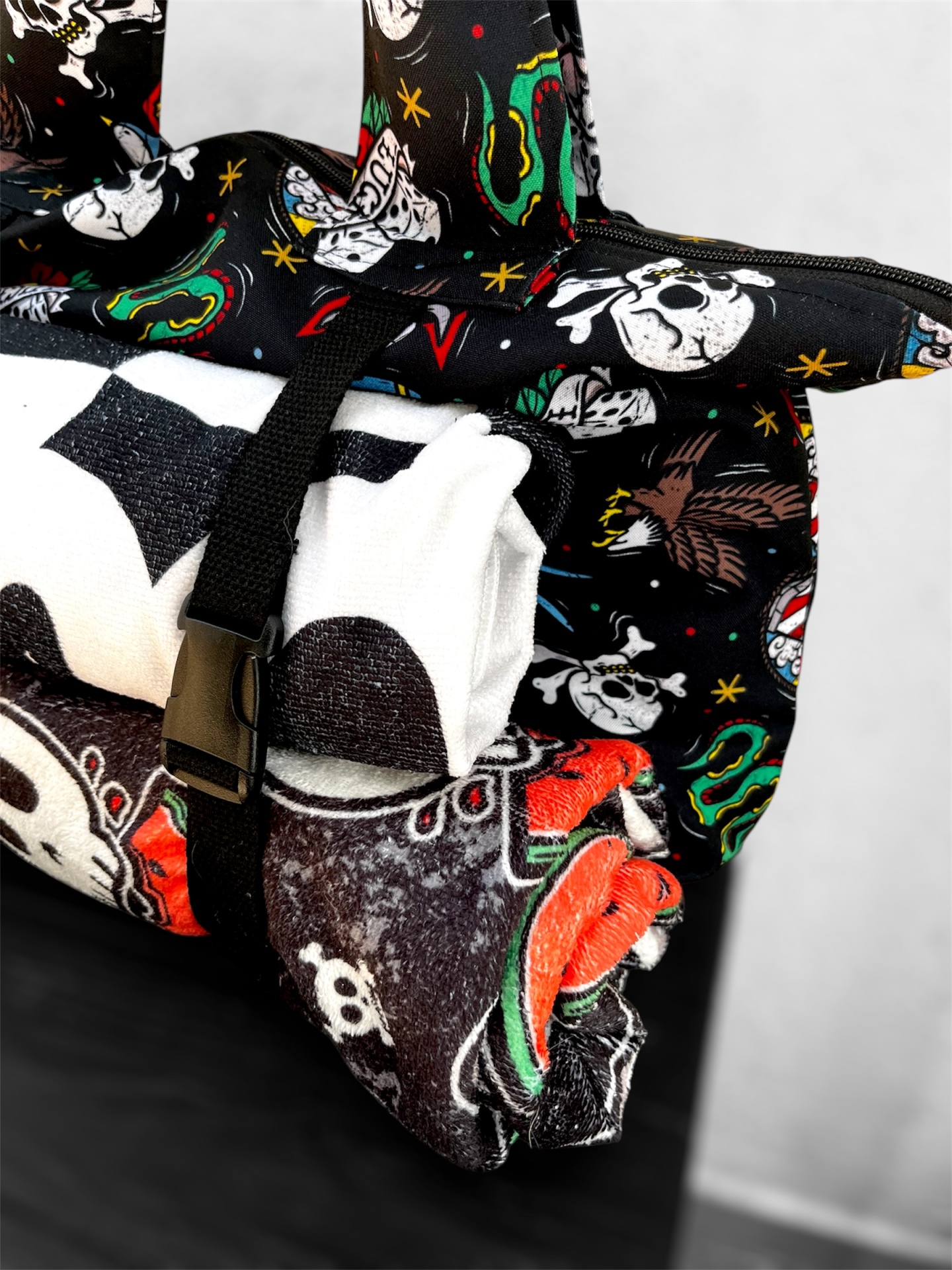 Saco preto com padrão de caveiras coloridas e cobertor dobrado com padrão de caveiras.