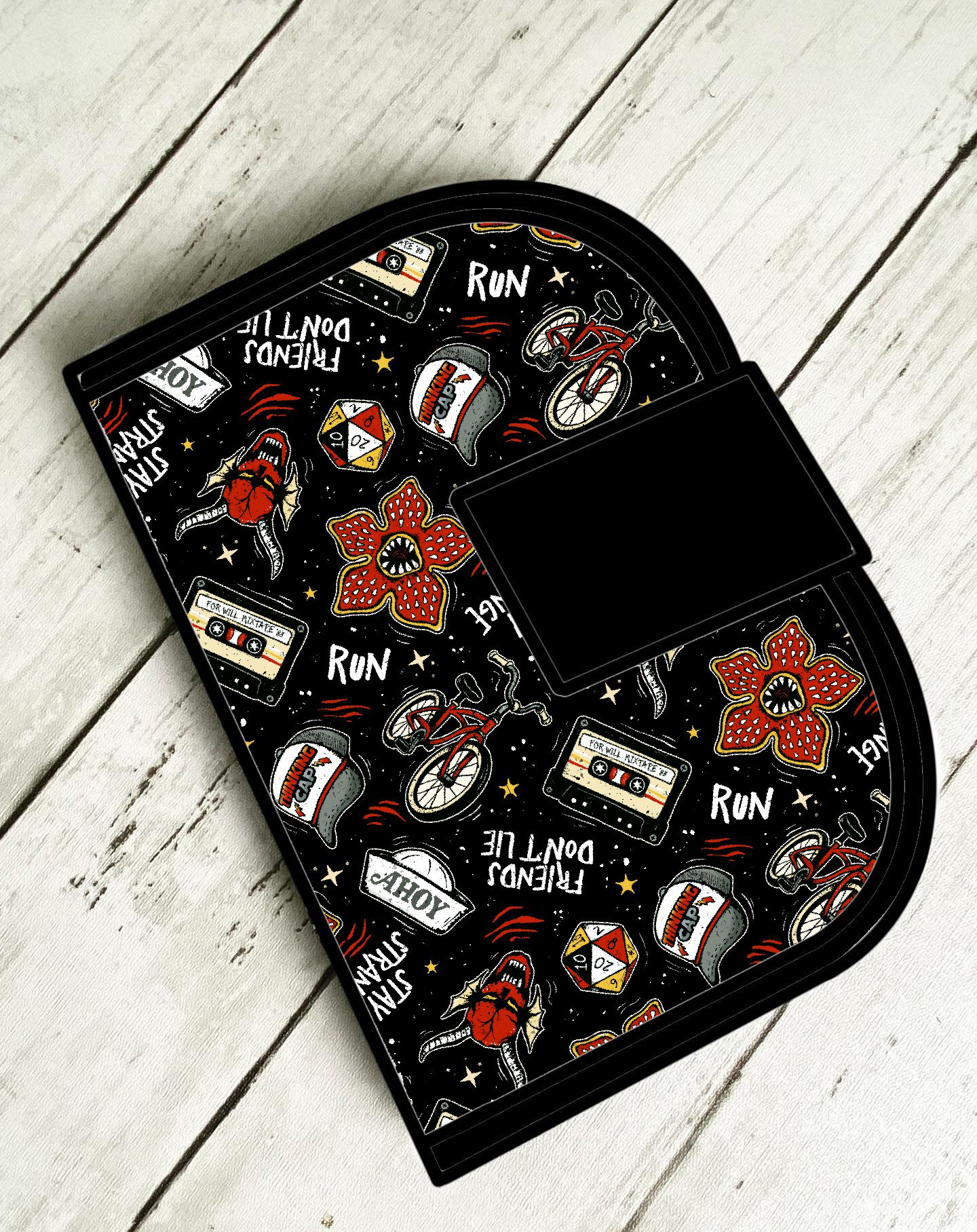 Carteira preta com estampas coloridas e textos em fundo de madeira clara