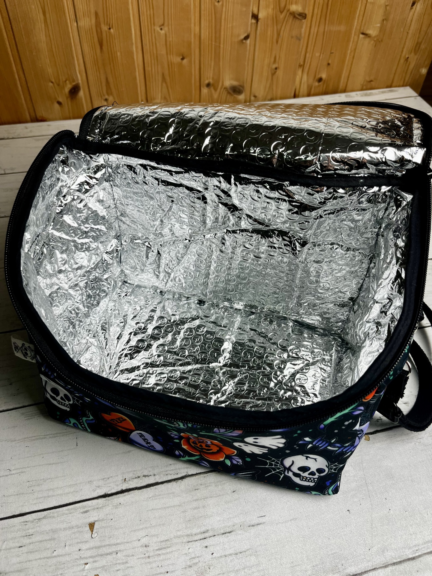 Bolsa térmica com padrão de caveiras e flores, interior prateado acolchoado