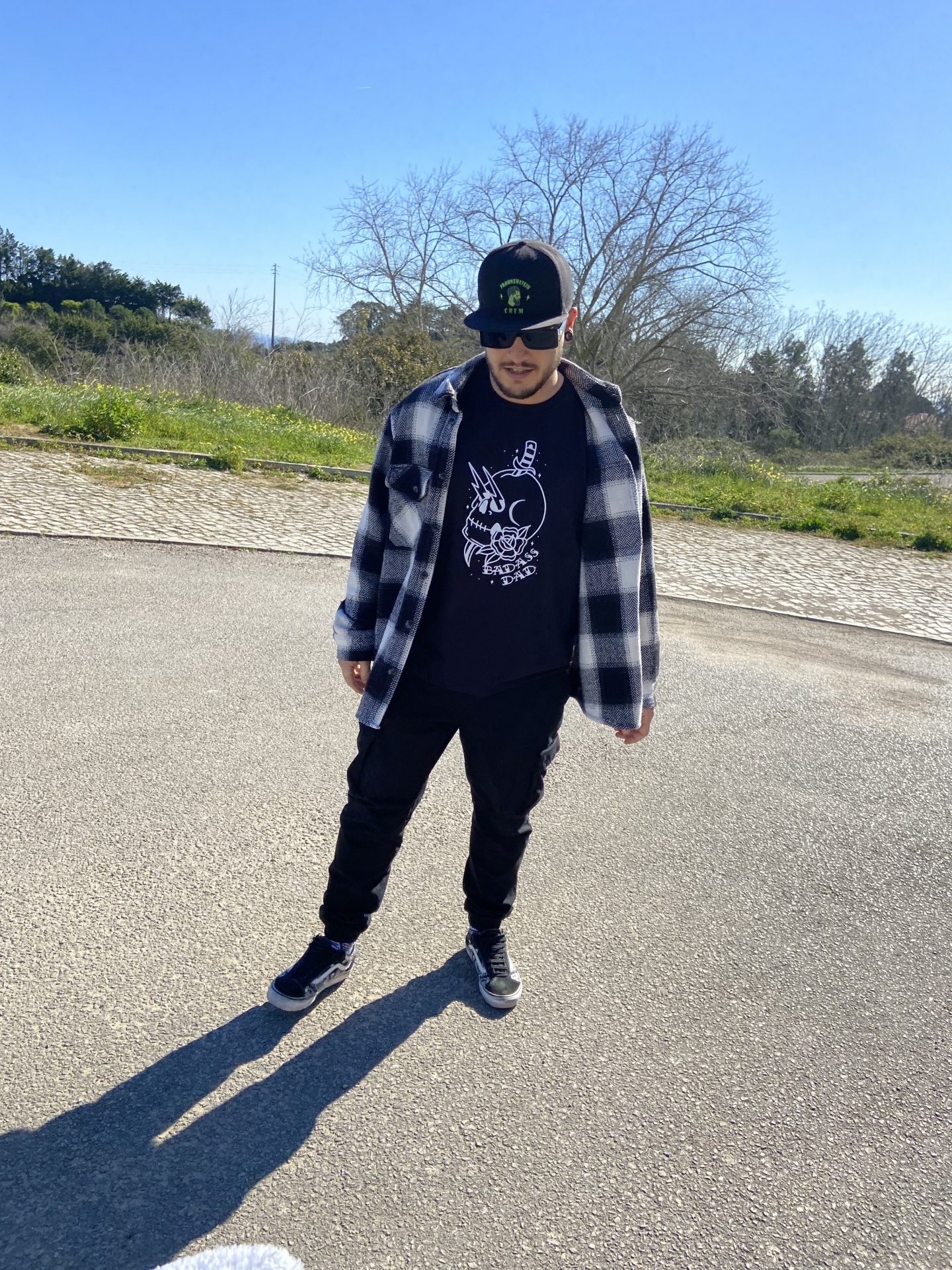 Homem com boné preto e camisa xadrez preta e branca ao ar livre