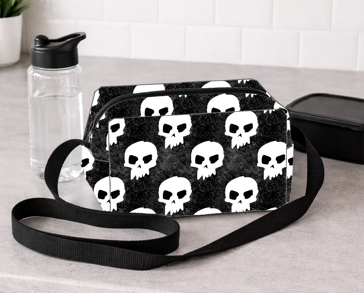 Bolsa tiracolo preta com padrão de caveiras brancas em bancada cinza