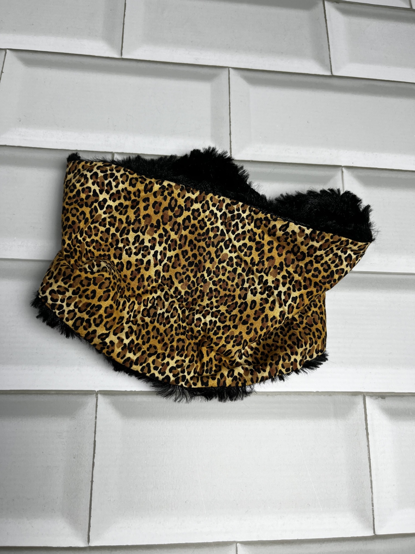 Cachecol com padrão de pele de leopardo e interior peludo preto sobre fundo de azulejos brancos