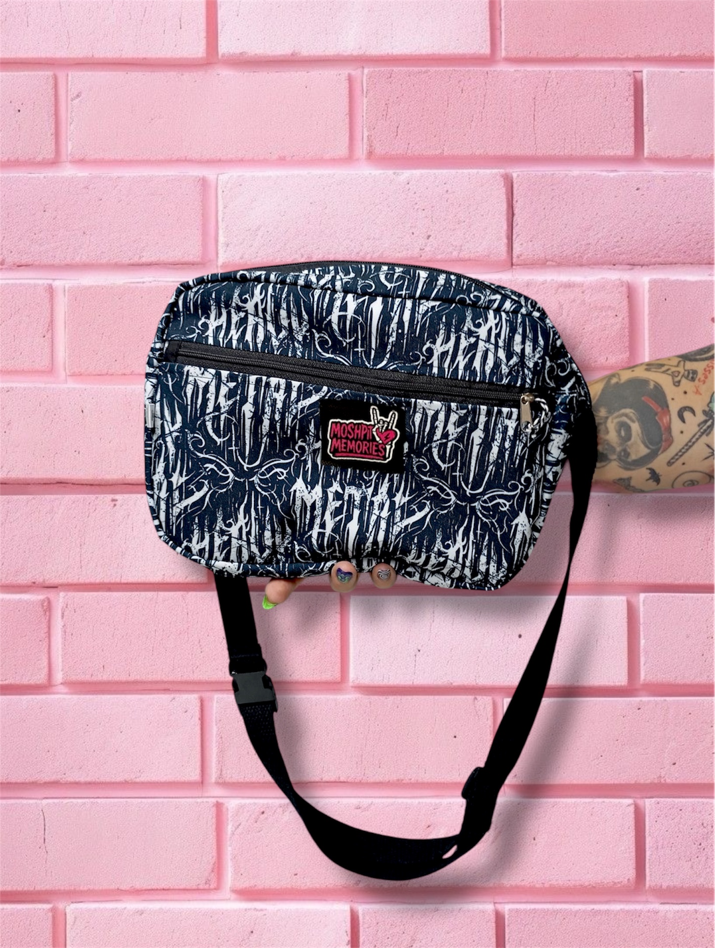 Pochete preta com padrão branco abstrato e logo MOSHPIT MEMORIES, com strap preto e fecho, em fundo de parede rosa