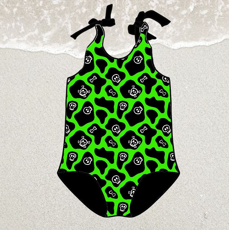 Fato de banho infantil verde com padrão de caveiras e ossos em areia à beira do mar