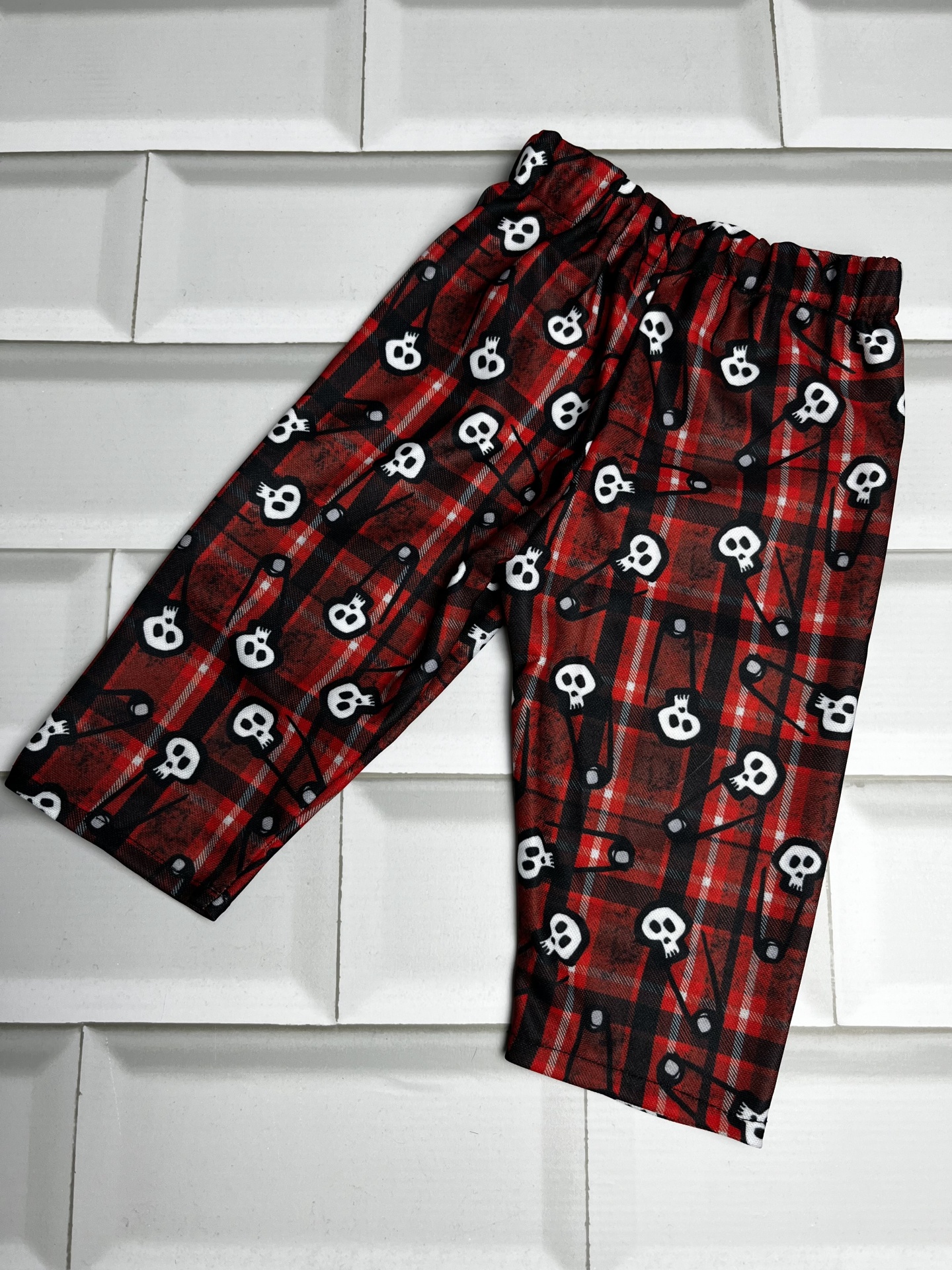 Calças com padrão xadrez vermelho e preto com caveiras brancas