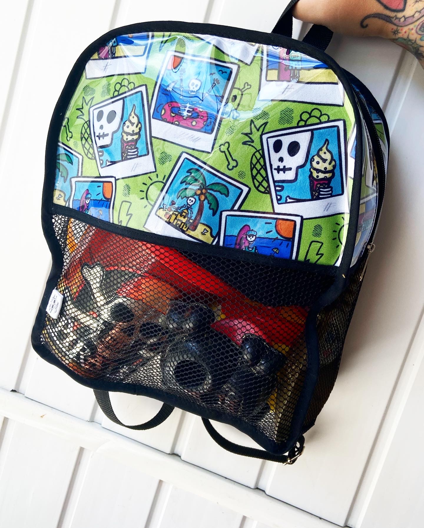 Mochila colorida com desenhos de caveiras e bolso frontal em malha preta com tubos pretos