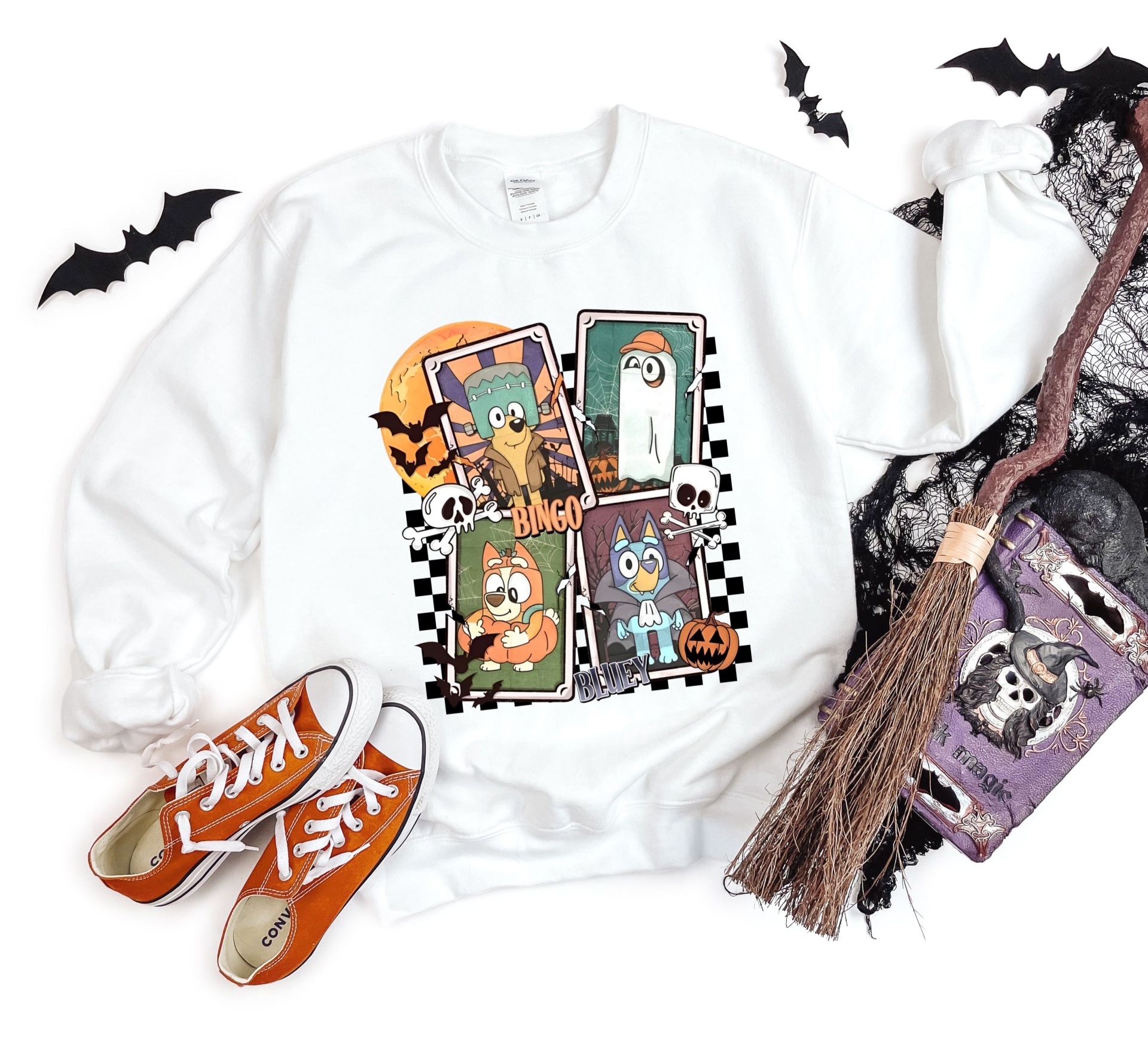 Sweatshirt branca com personagens animados e motivos de Halloween, sapatos laranja, vassoura e sacola roxa com caveira