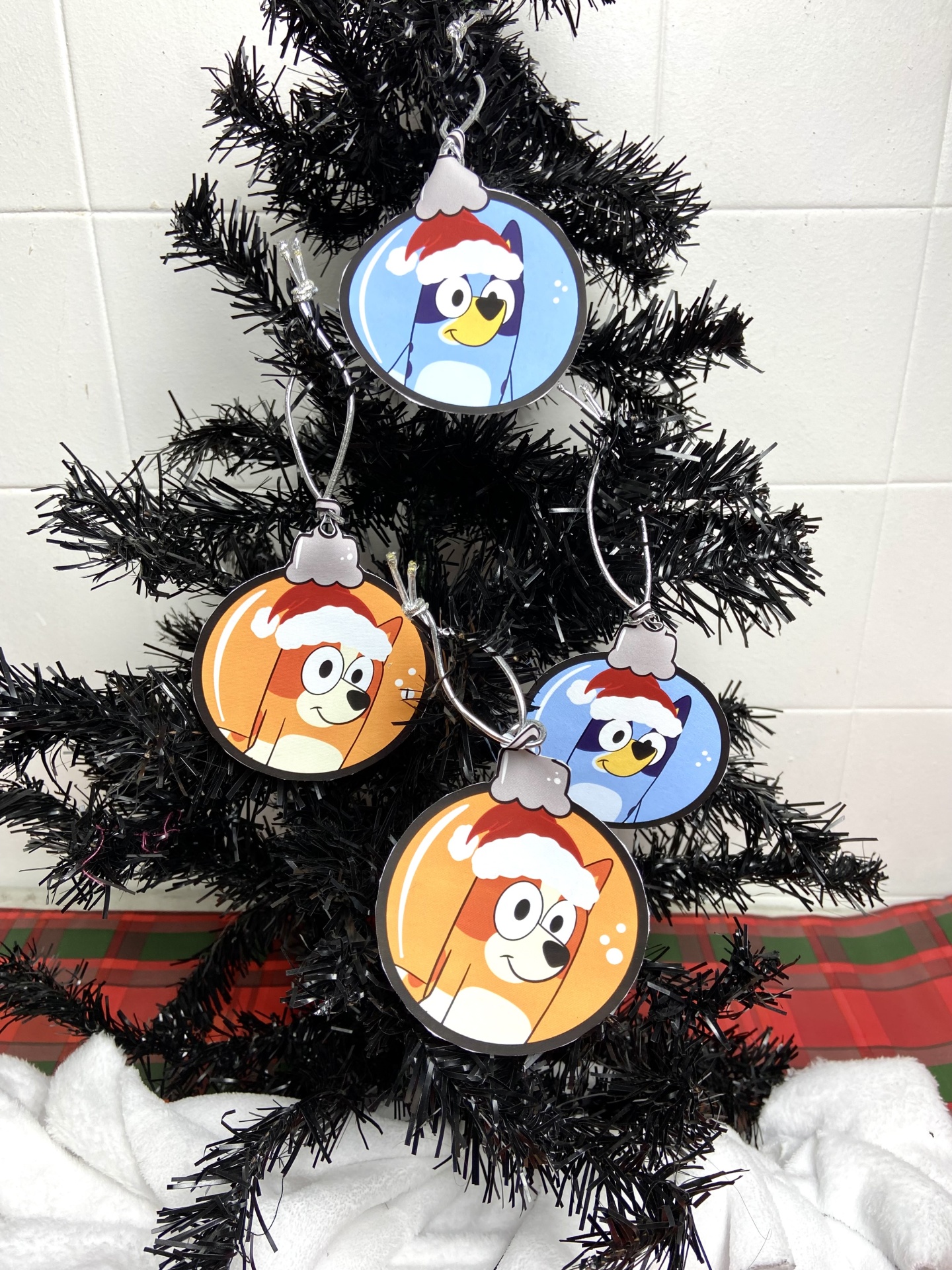 Ornamentos de Natal redondos com personagens de desenho animado pendurados numa árvore preta.