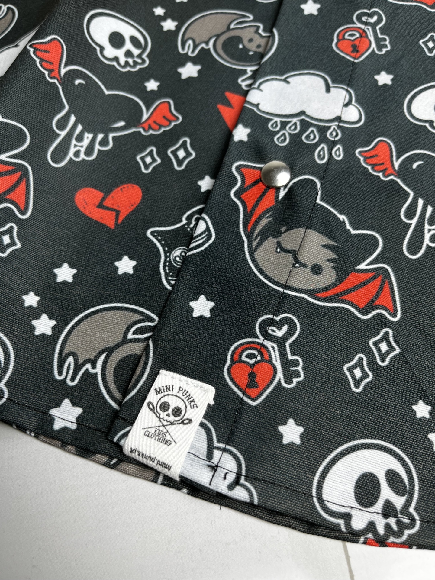 Tecido preto com desenhos coloridos de caveiras e morcegos, etiqueta MINI PUNKS CLOTHING