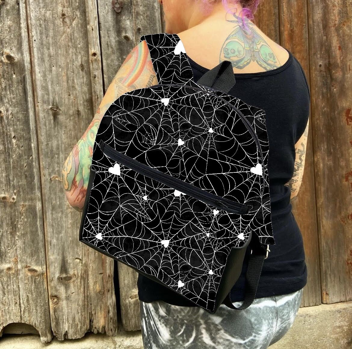 Mochila preta com padrão de teias de aranha e estrelas brancas usada por pessoa com tatuagens