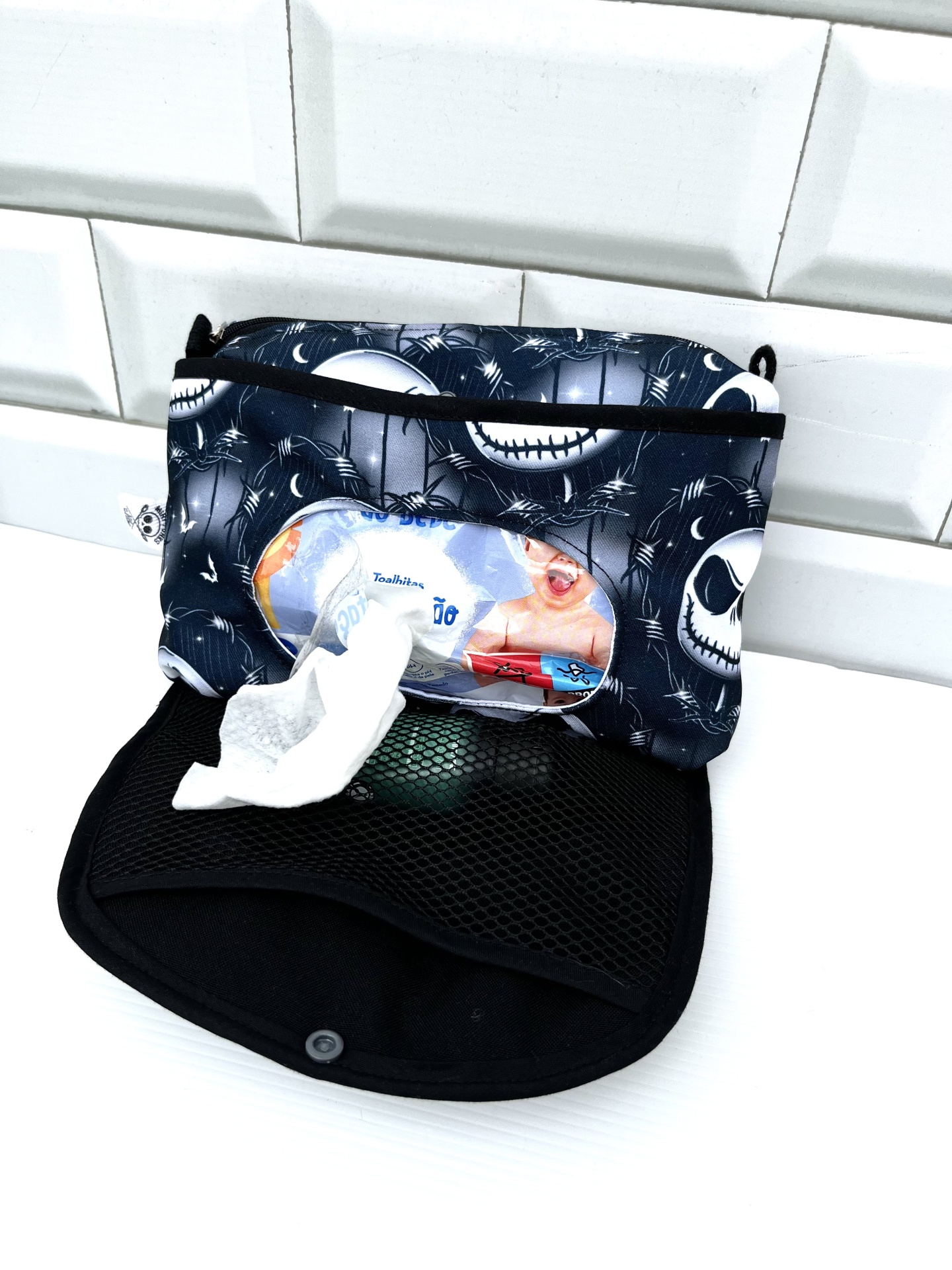 Estojo de tecido com padrão de caveiras e aranhas a preto e branco e toalhitas húmidas visíveis