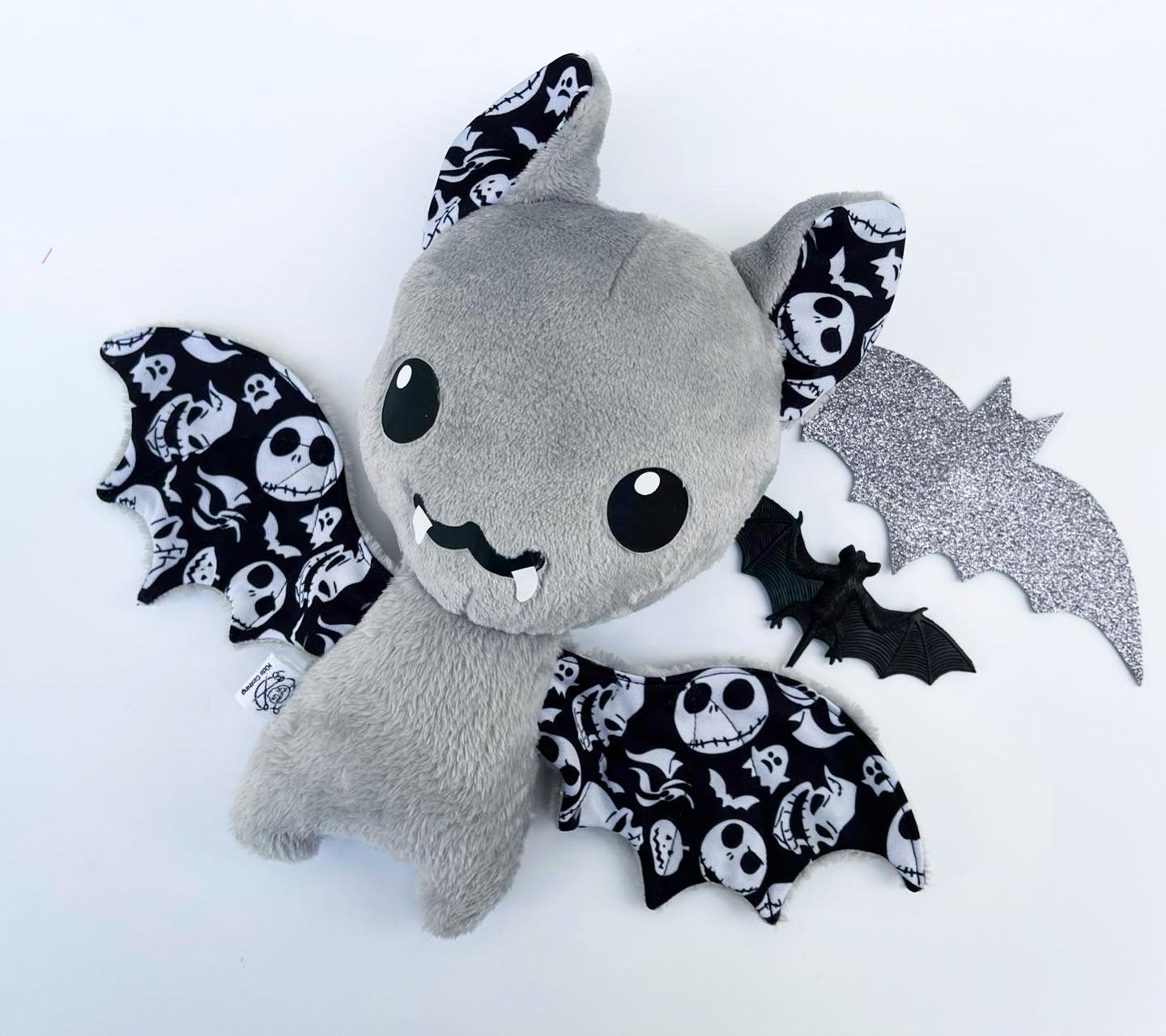 Pelúcia morcego cinzento com asas com padrão de caveiras e asa prateada