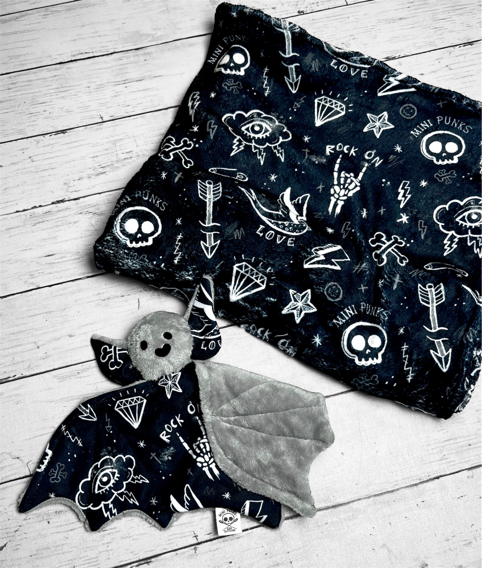 Cobertor e pelúcia morcego com padrão punk em preto e branco sobre chão de madeira clara