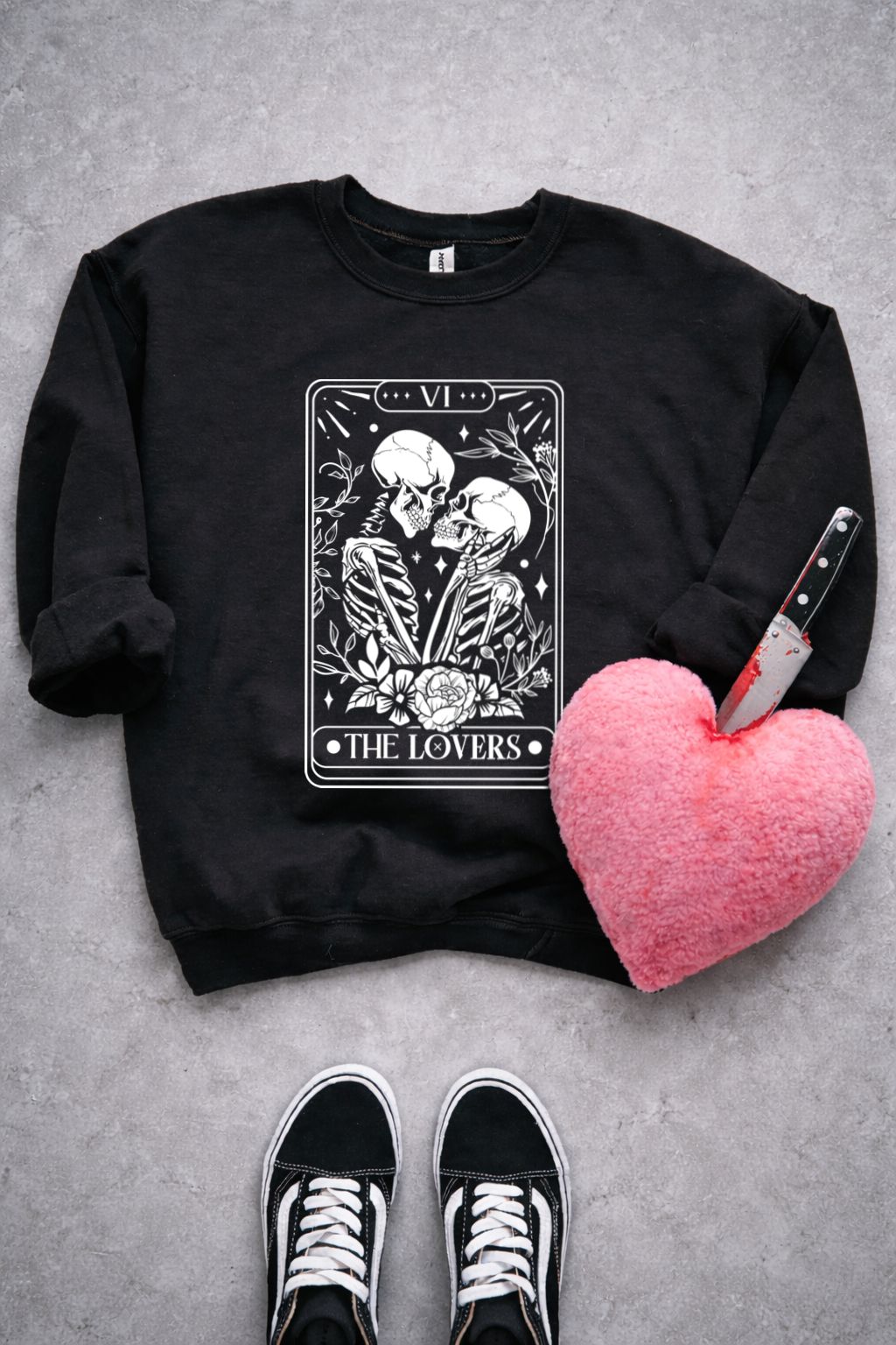 Sweatshirt preta com estampa de esqueletos e coração de peluche rosa com faca espetada