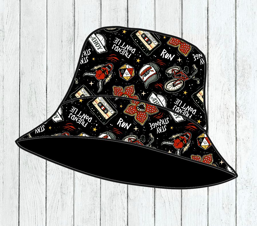 Chapéu bucket preto com diversas estampas coloridas e frases em branco sobre fundo de madeira clara.