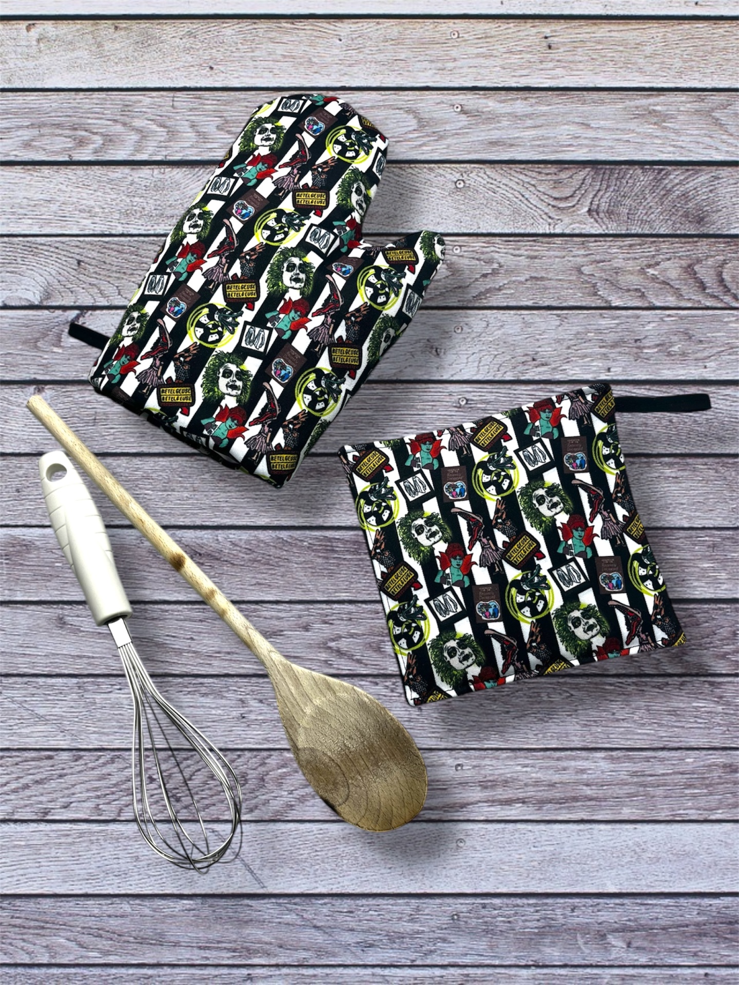 Conjunto de luvas de forno e suporte para panelas com padrão colorido sobre superfície de madeira clara, junto com utensílios de cozinha.