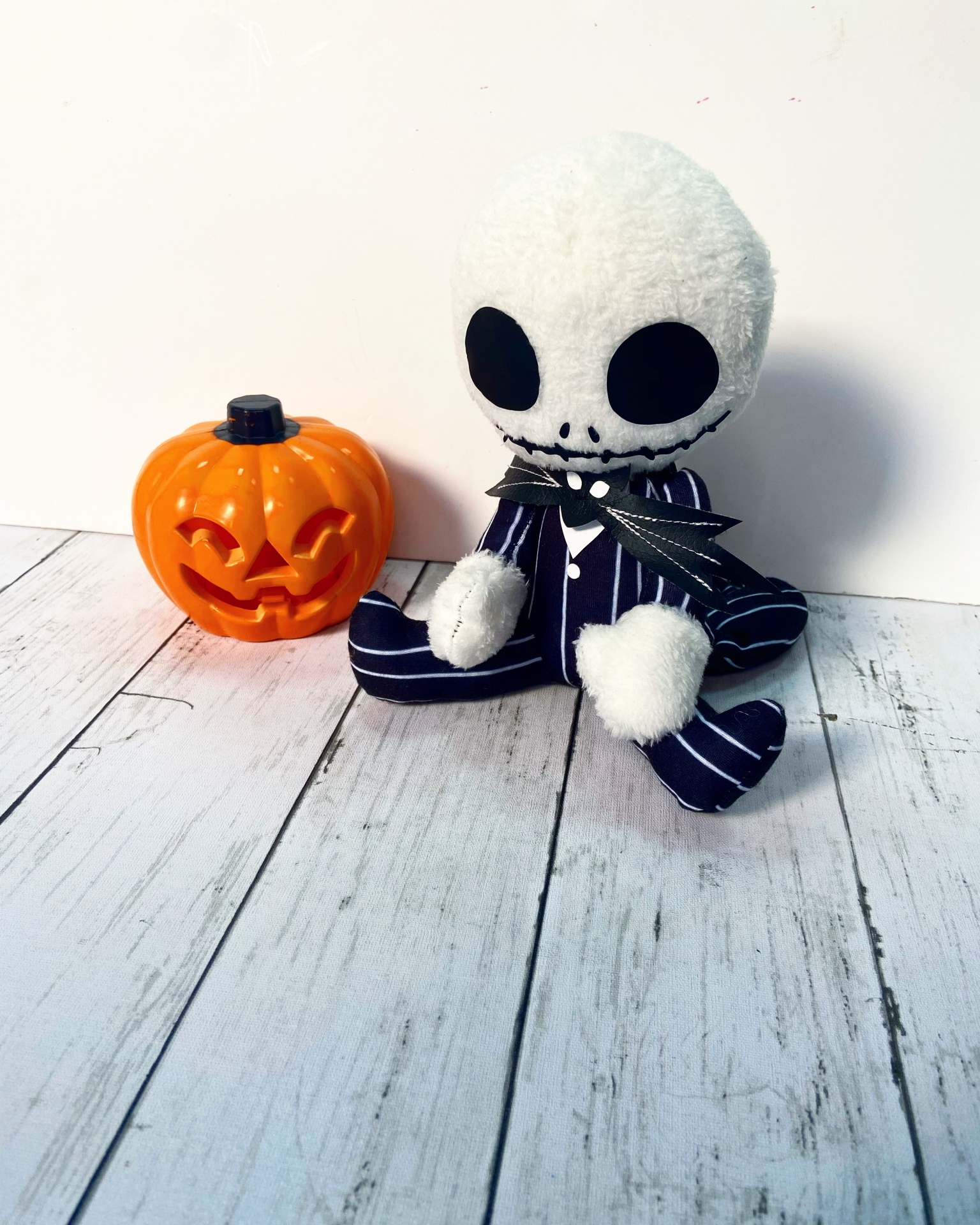 Boneco de peluche com cabeça branca e olhos pretos sentado ao lado de abóbora de plástico laranja