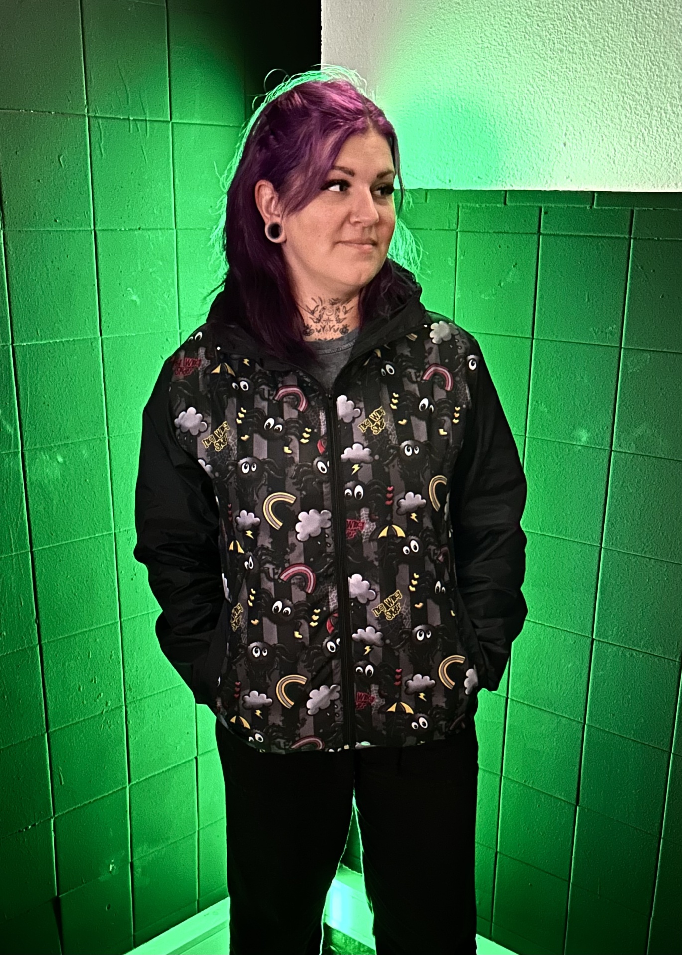 Pessoa a usar casaco colorido com padrão de olhos e nuvens num espaço com azulejos verdes