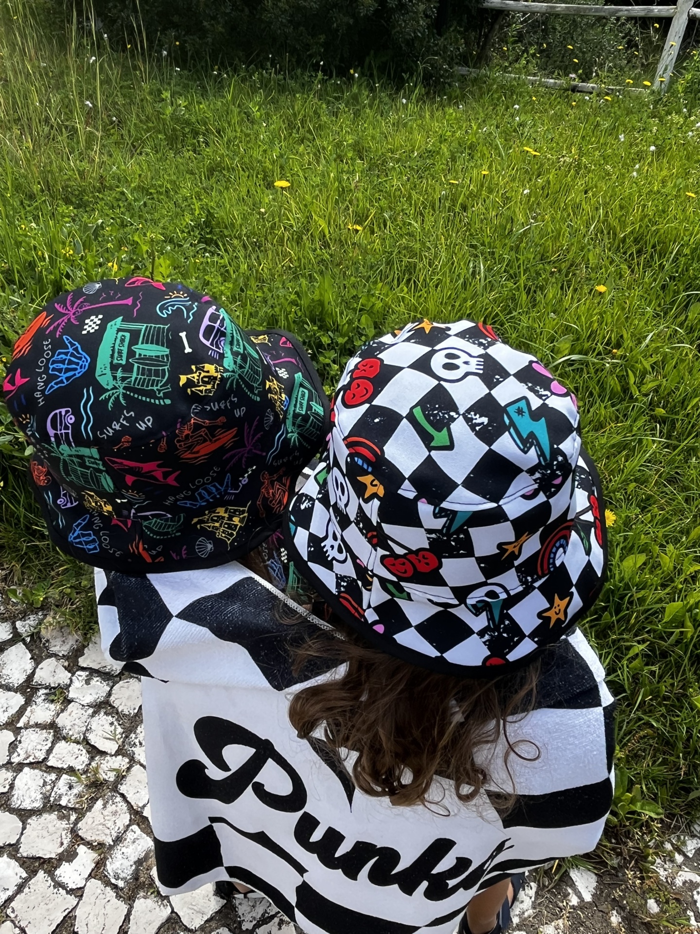 Dois chapéus bucket coloridos usados ao ar livre com relva e calçada de pedras