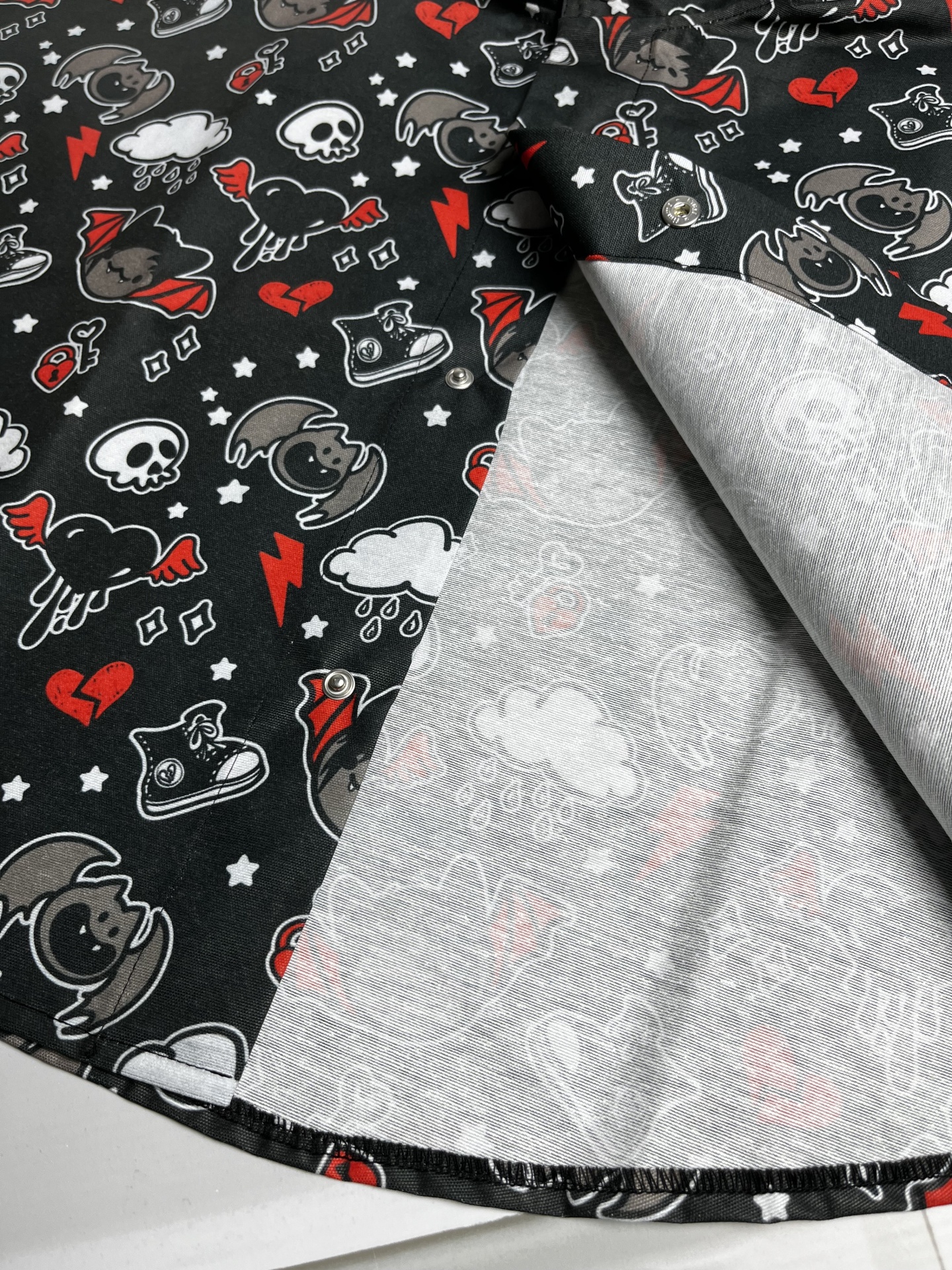 Tecido preto com padrão colorido de caveiras, corações partidos e cães com asas