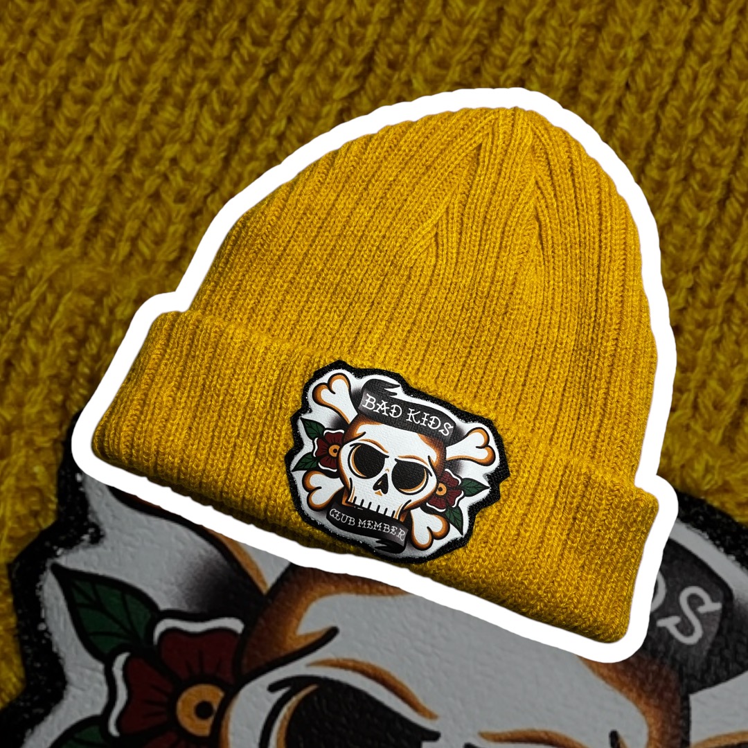 Gorro amarelo mostarda com etiqueta de caveira 'BAD KIDS CLUB MEMBER'