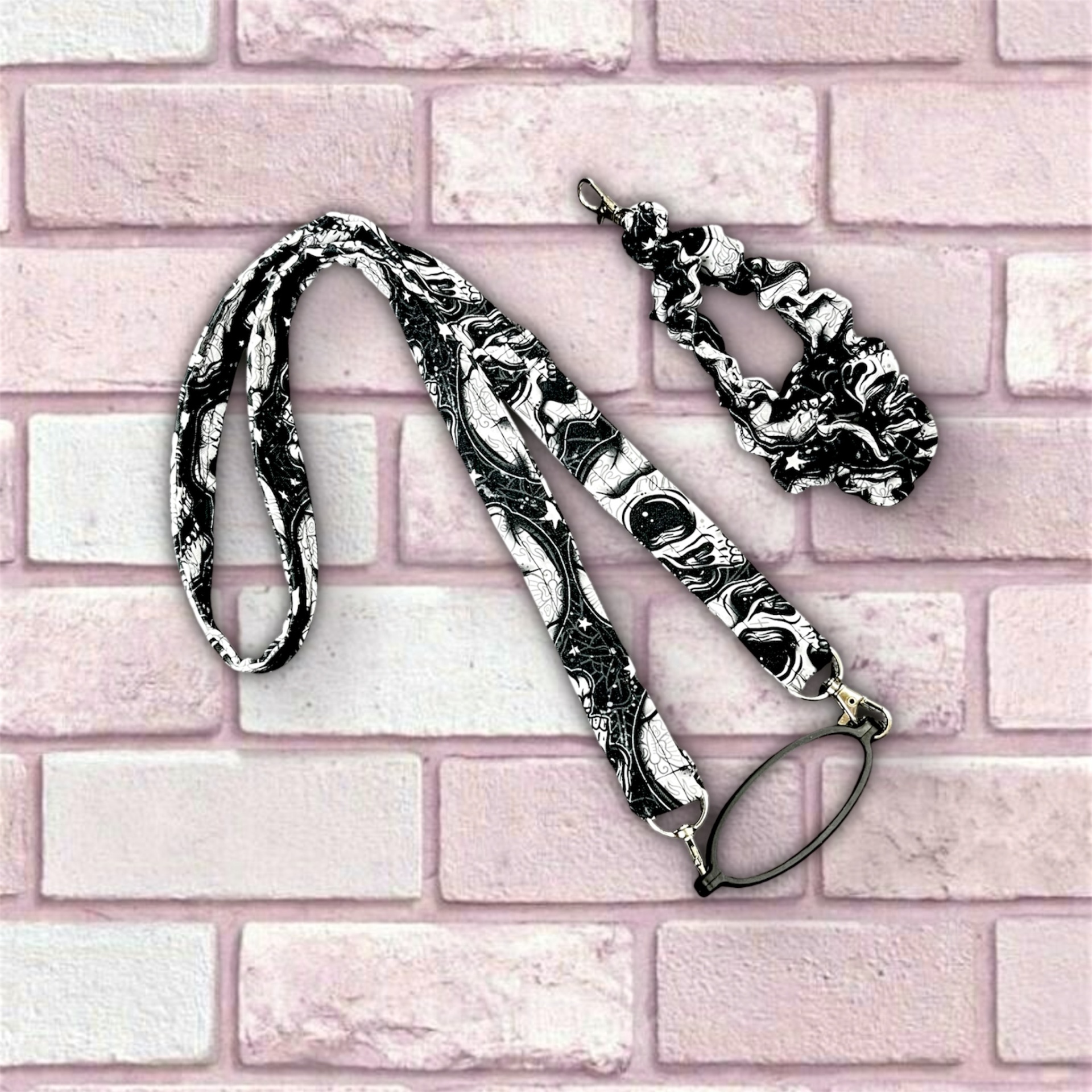 Estojo porta óculos e porta chaves com padrão preto e branco sobre fundo de tijolos rosa