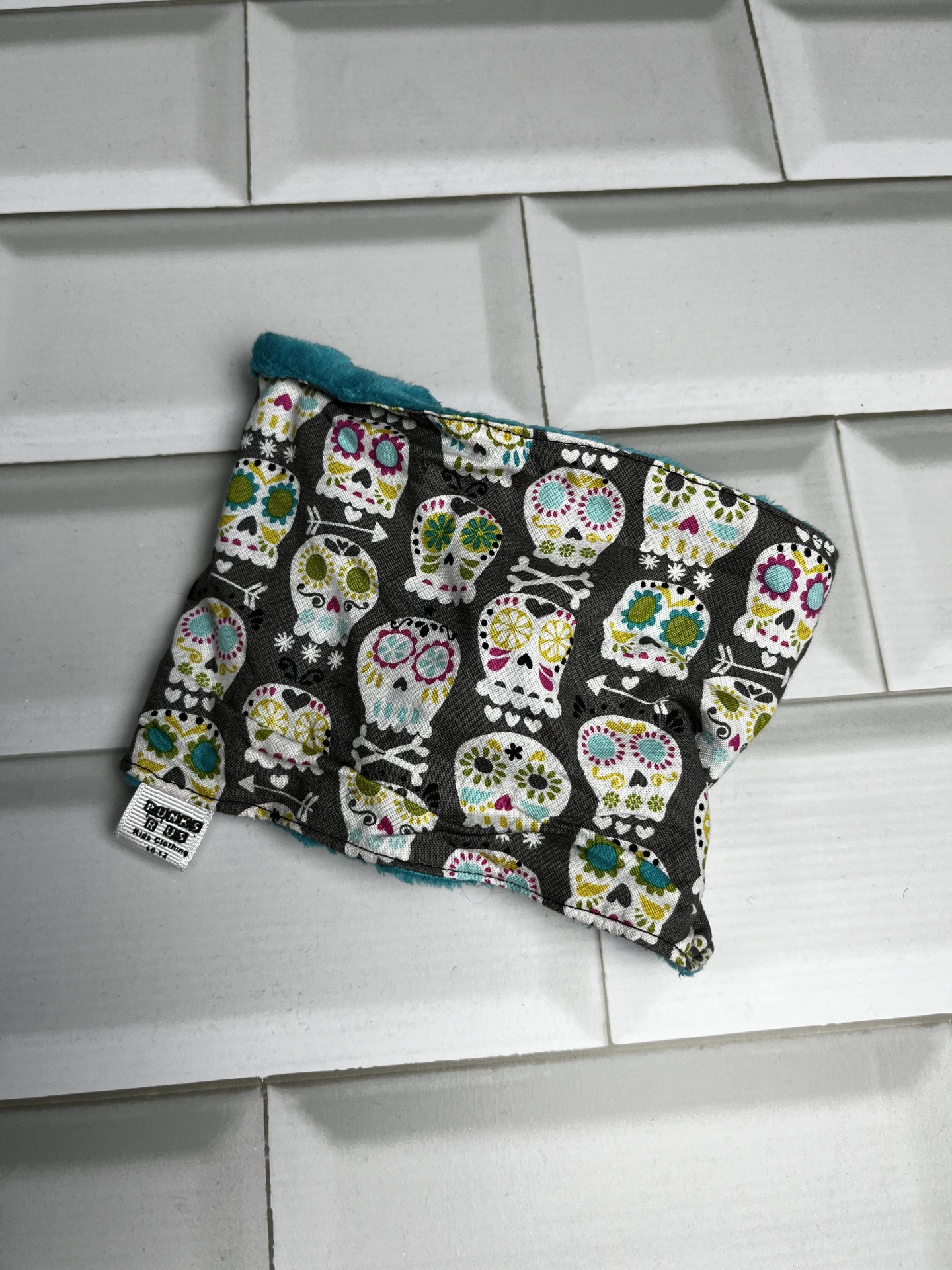 Peça de tecido macio com padrão colorido de caveiras em fundo preto